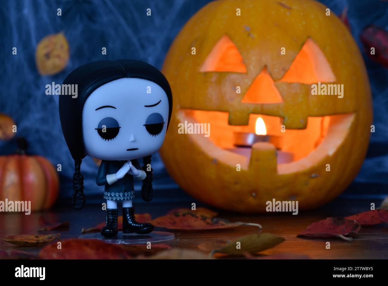 Funko Pop action figure of Wednesday Addams from animated film The Addams family. Halloween, Jack o lantern, spider web, autumn leaves, decor, spooky. Stock Photo