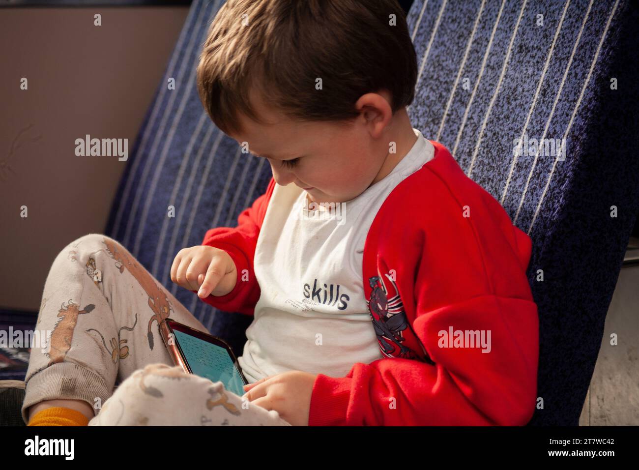 Tech-Savvy Journey: A 6-year-old boy engrossed in his smartphone games during a train ride, his angelic face filled with concentration. Stock Photo