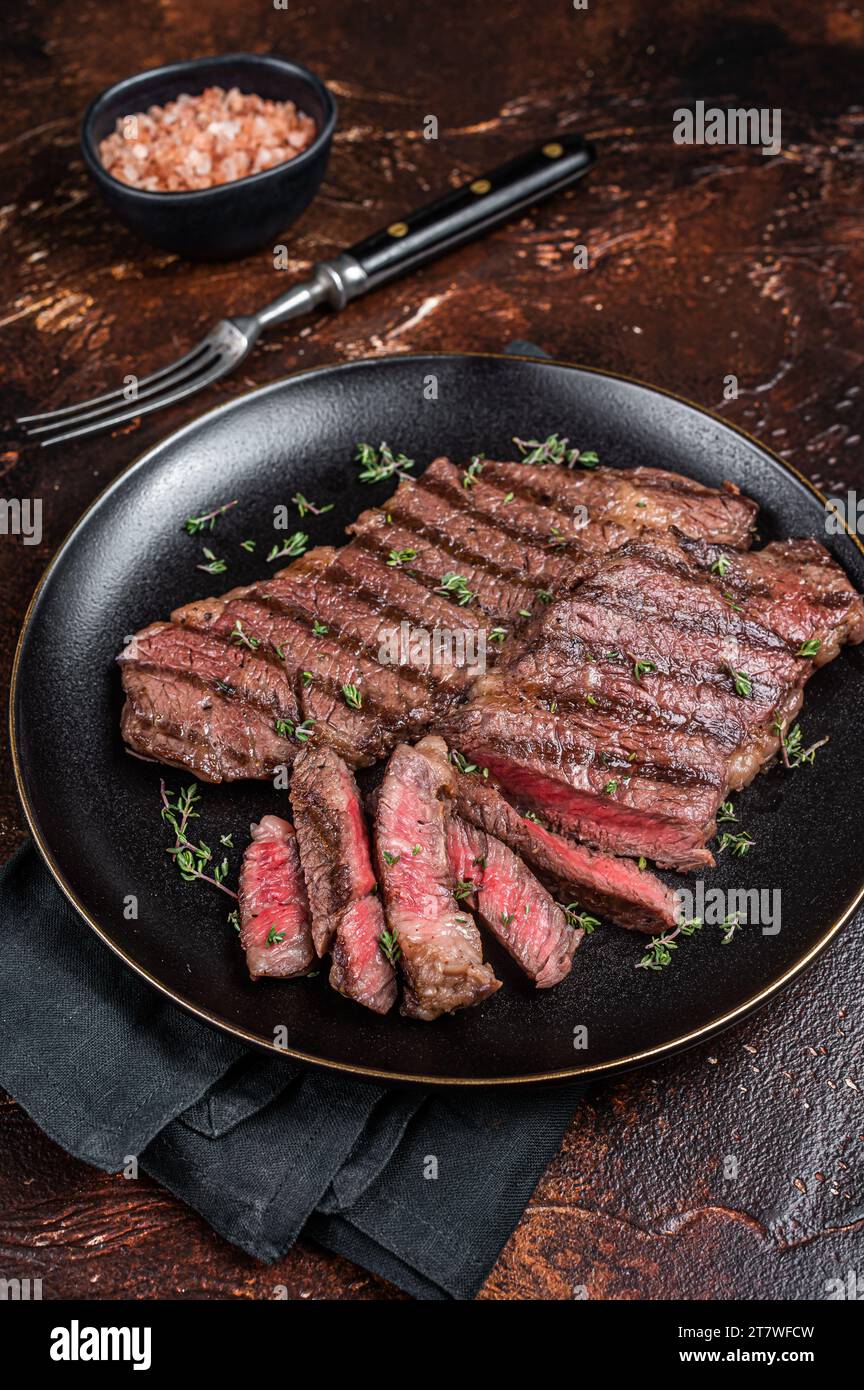 Barbecue denver strip beef meat steak on a plate. Dark background. Top view. Stock Photo