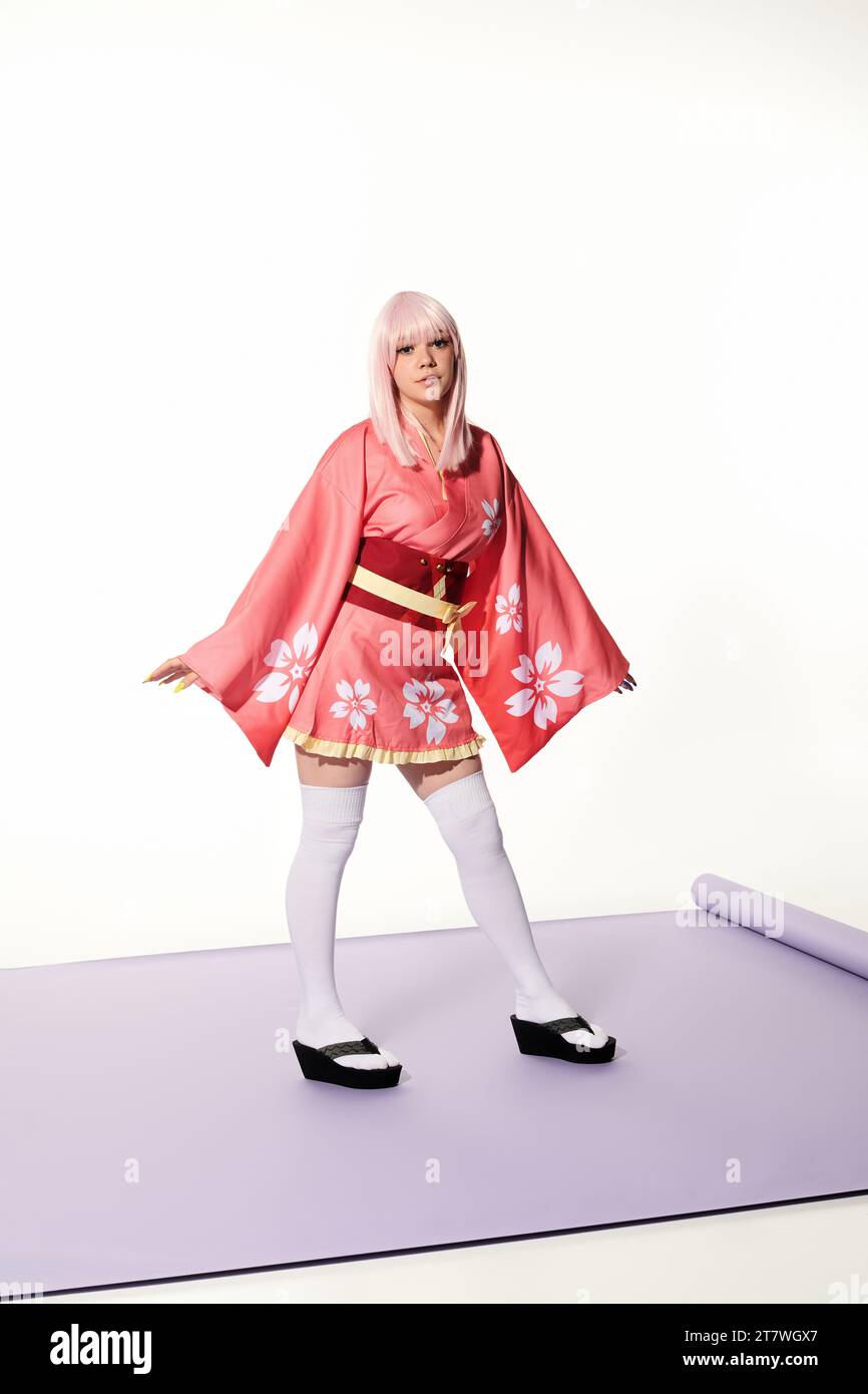 japanese cosplay subculture, blonde woman in kimono and wig on purple carper and white backdrop Stock Photo