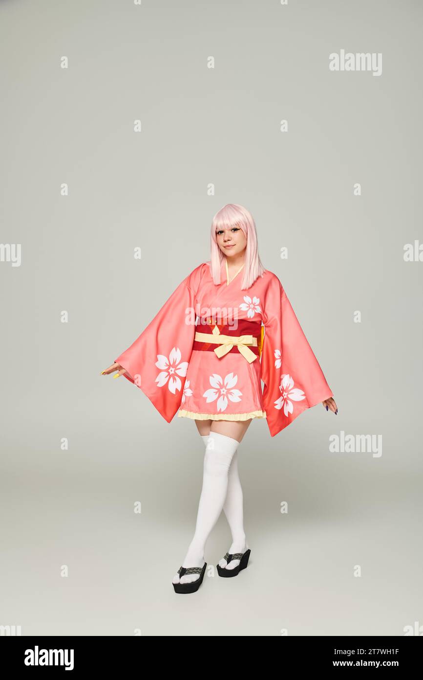 full length of young anime woman in blonde wig and pink kimono on grey, japanese subculture Stock Photo