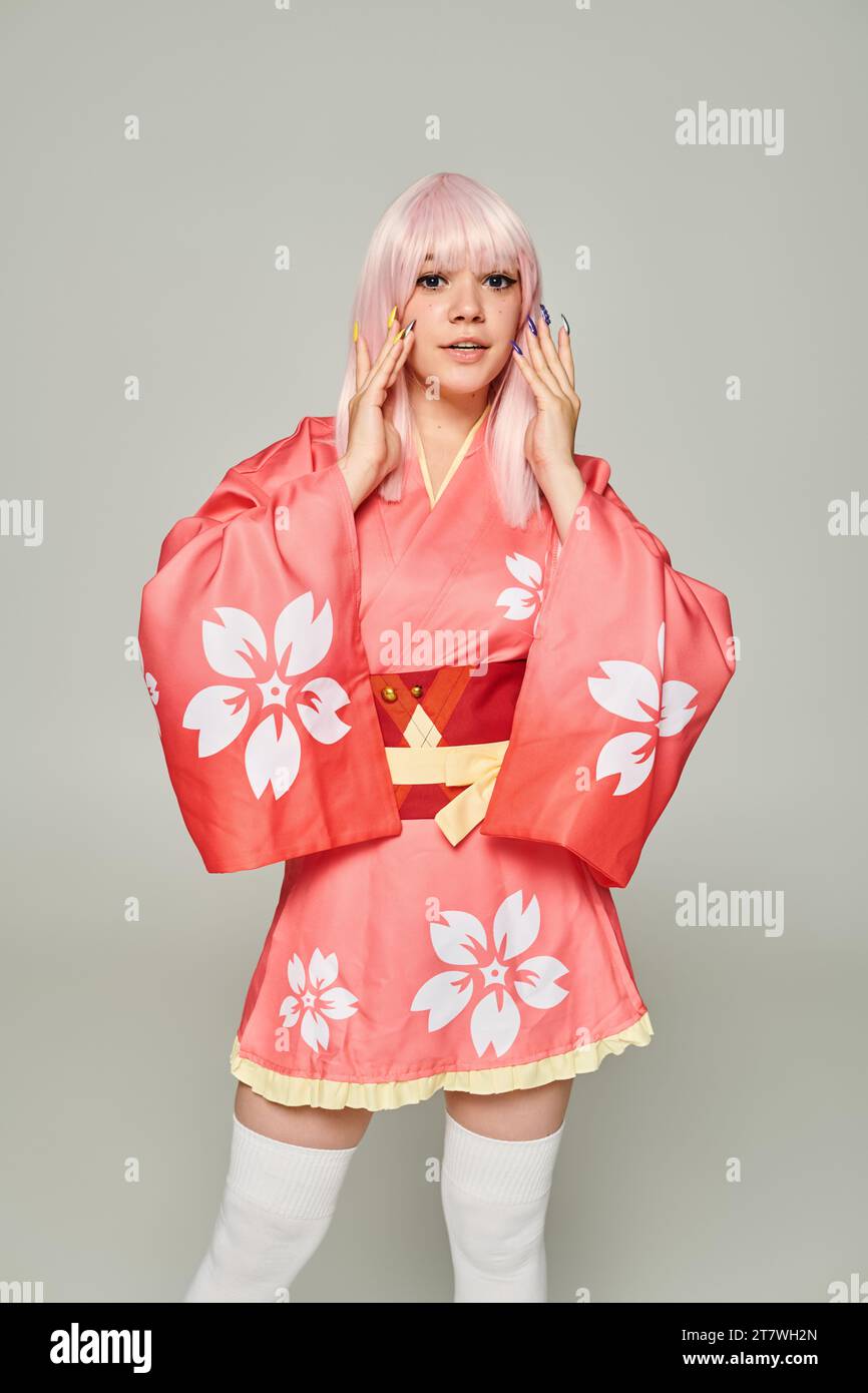 young blonde woman with colorful manicure wearing pink kimono and looking at camera on grey Stock Photo