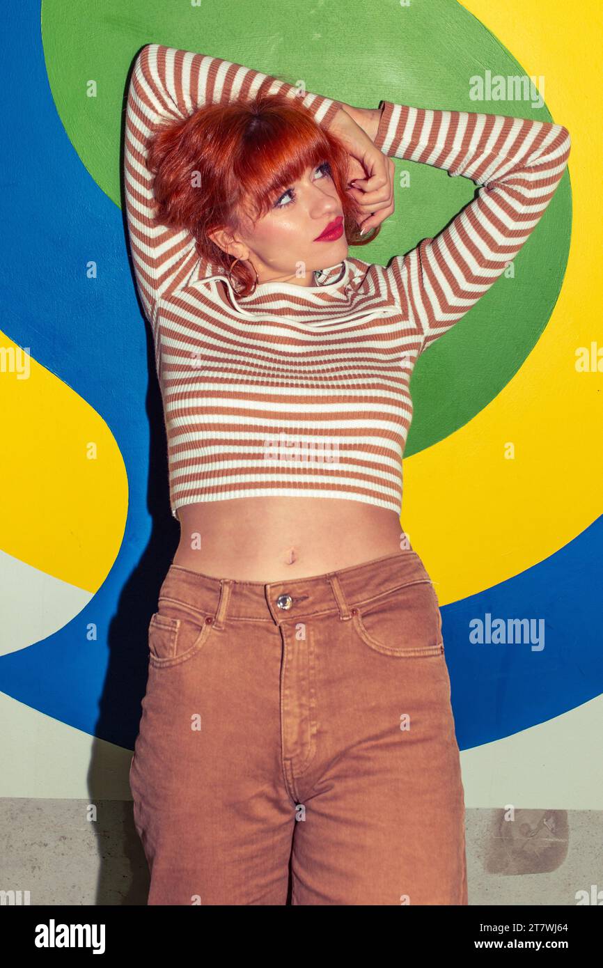 Young redhead Caucasian woman in retro style of 70s posing at colorful wall looking up Stock Photo