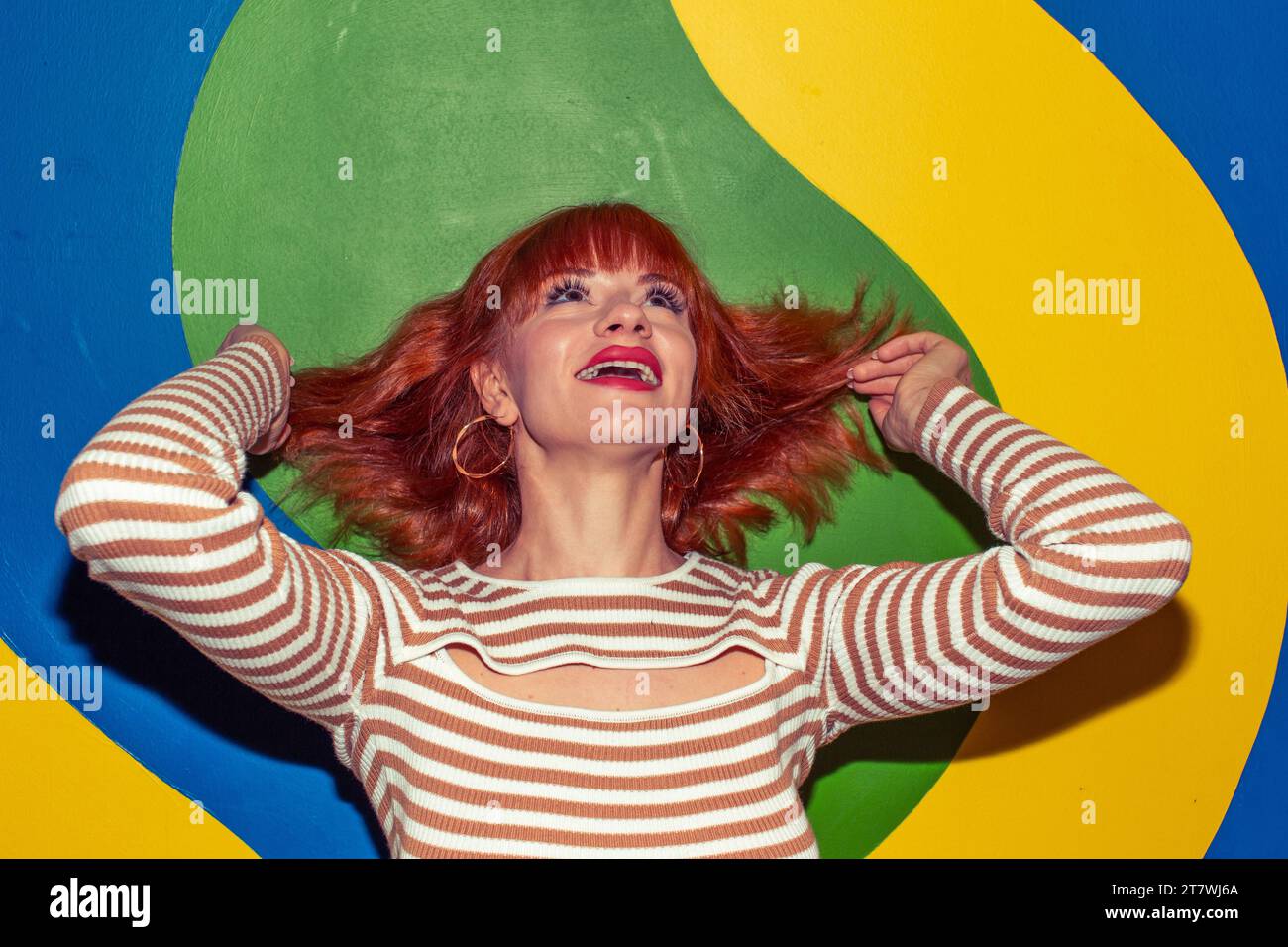 Happy young redhead Caucasian woman in retro style of 70s posing at colorful wall Stock Photo