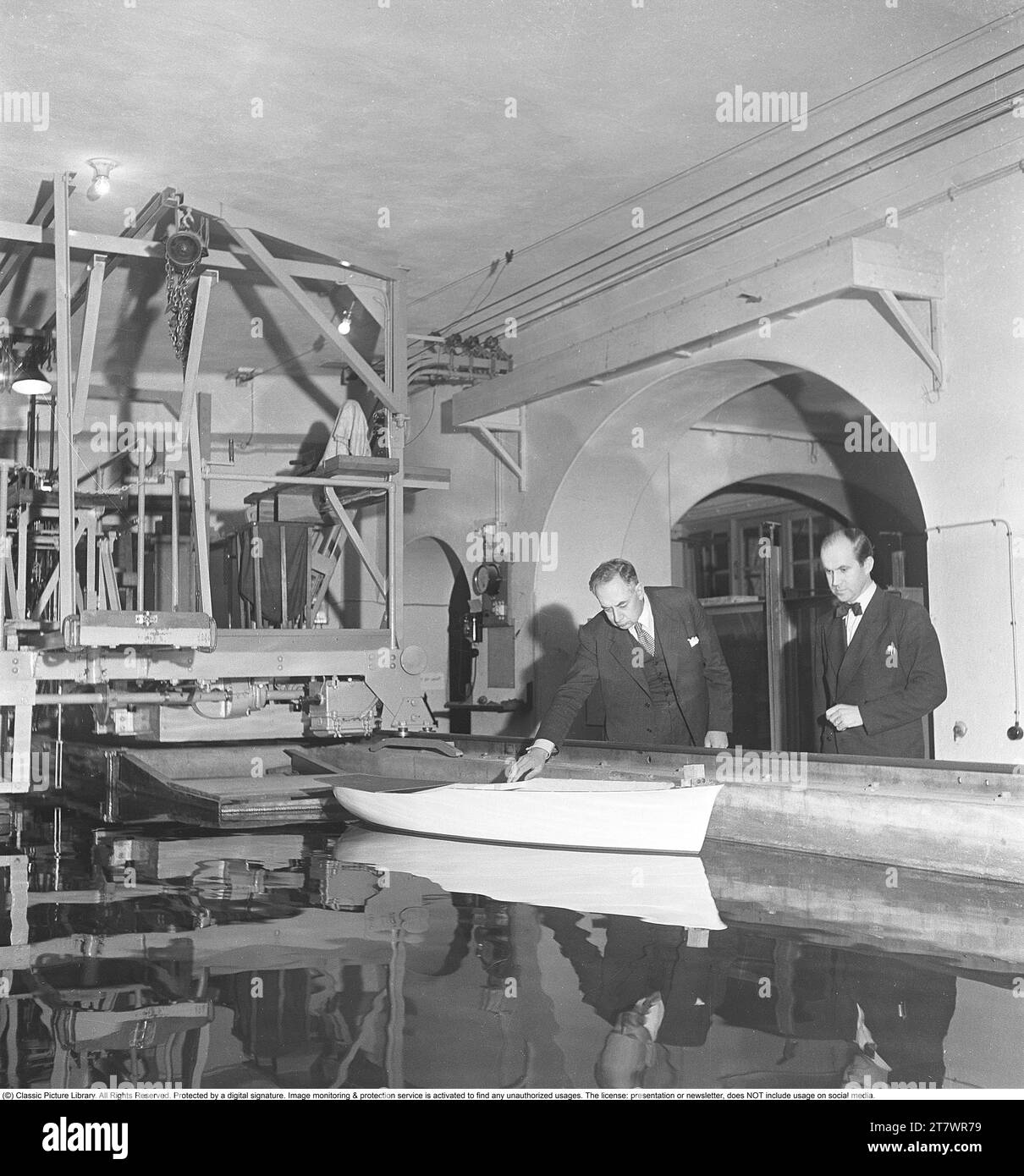 Advanced laboratory experiments in the 1940s. Interior of a room where a model ship lies in a pool of water. When the ship model is pulled forward on the surface of the water in the basin, one studies how the surge waves and how the ship behaves and whether the hull design is successful or not. The test is necessary to test safety, design, eco-economy and performance, and affects how the ship will ultimately look and how the hull will be constructed. Sweden 1949. Kristoffersson ref AU51-3 Stock Photo