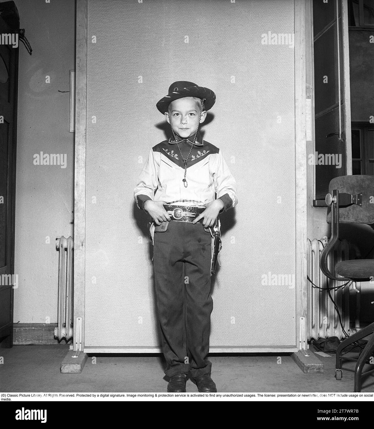 Boy in the 1950s. A boy is dressed in cowboy clothes, shirt, gun holster and cowboy hat and holds two toy revolvers. 1950. Kristoffersson ref AZ47-9 Stock Photo