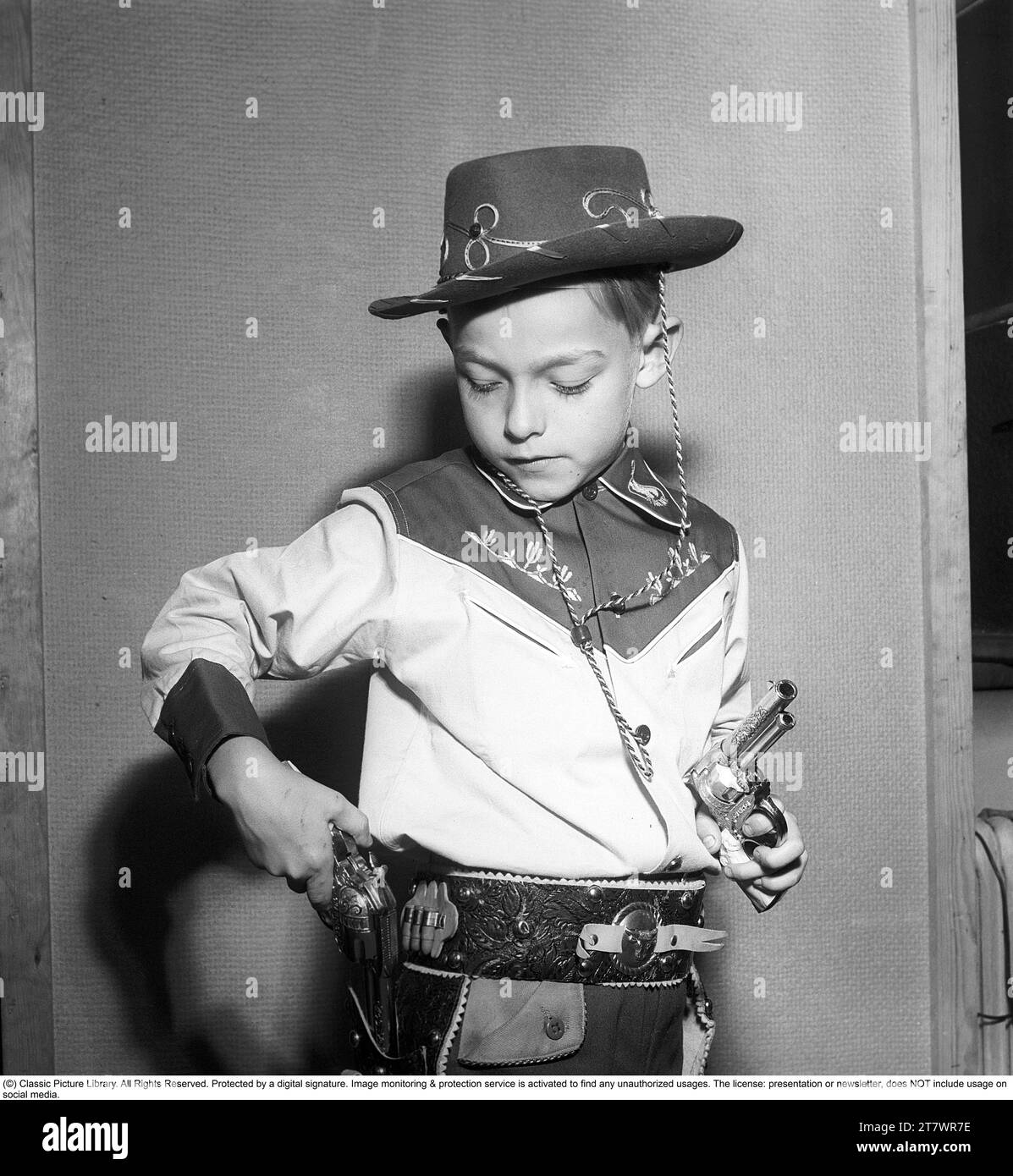 Boy in the 1950s. A boy is dressed in cowboy clothes, shirt, gun holster and cowboy hat and holds two toy revolvers. 1950. Kristoffersson ref AZ47-7 Stock Photo