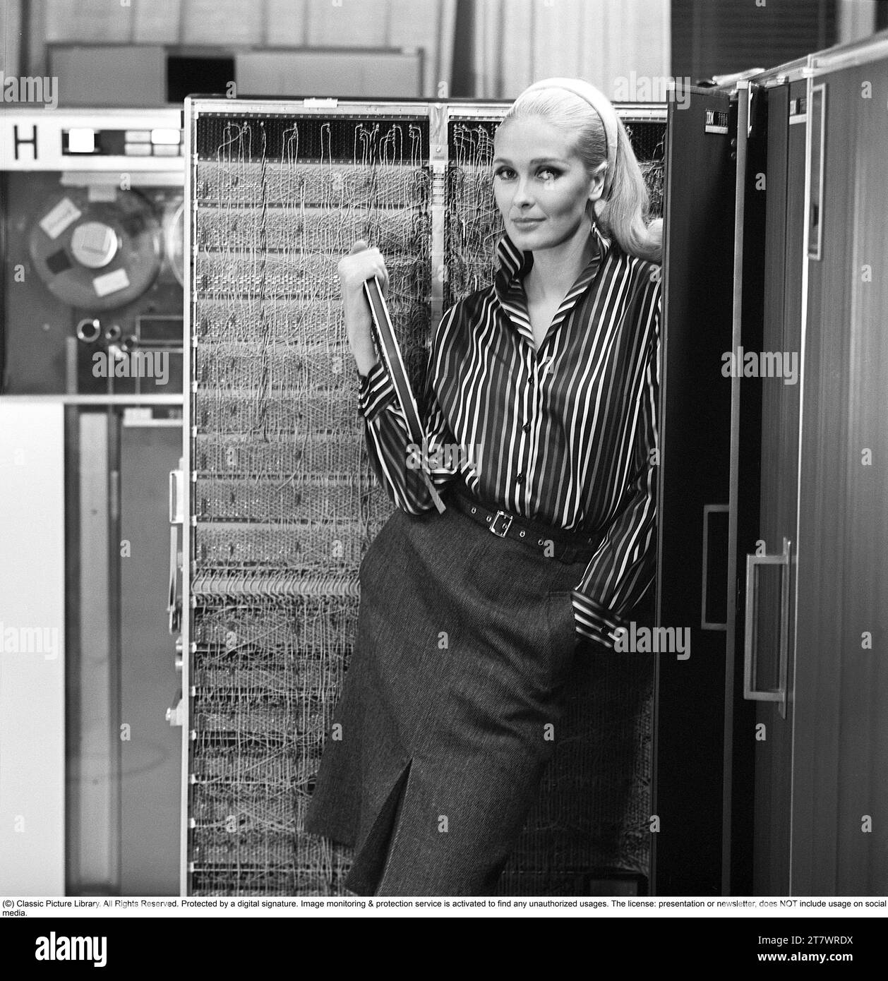 In the 1960s. Fashion model wearing the typical clothes of 1965. The photograph is taken in a 1960s mainframe computer room. Picture taken 1965. ref DV16 Stock Photo