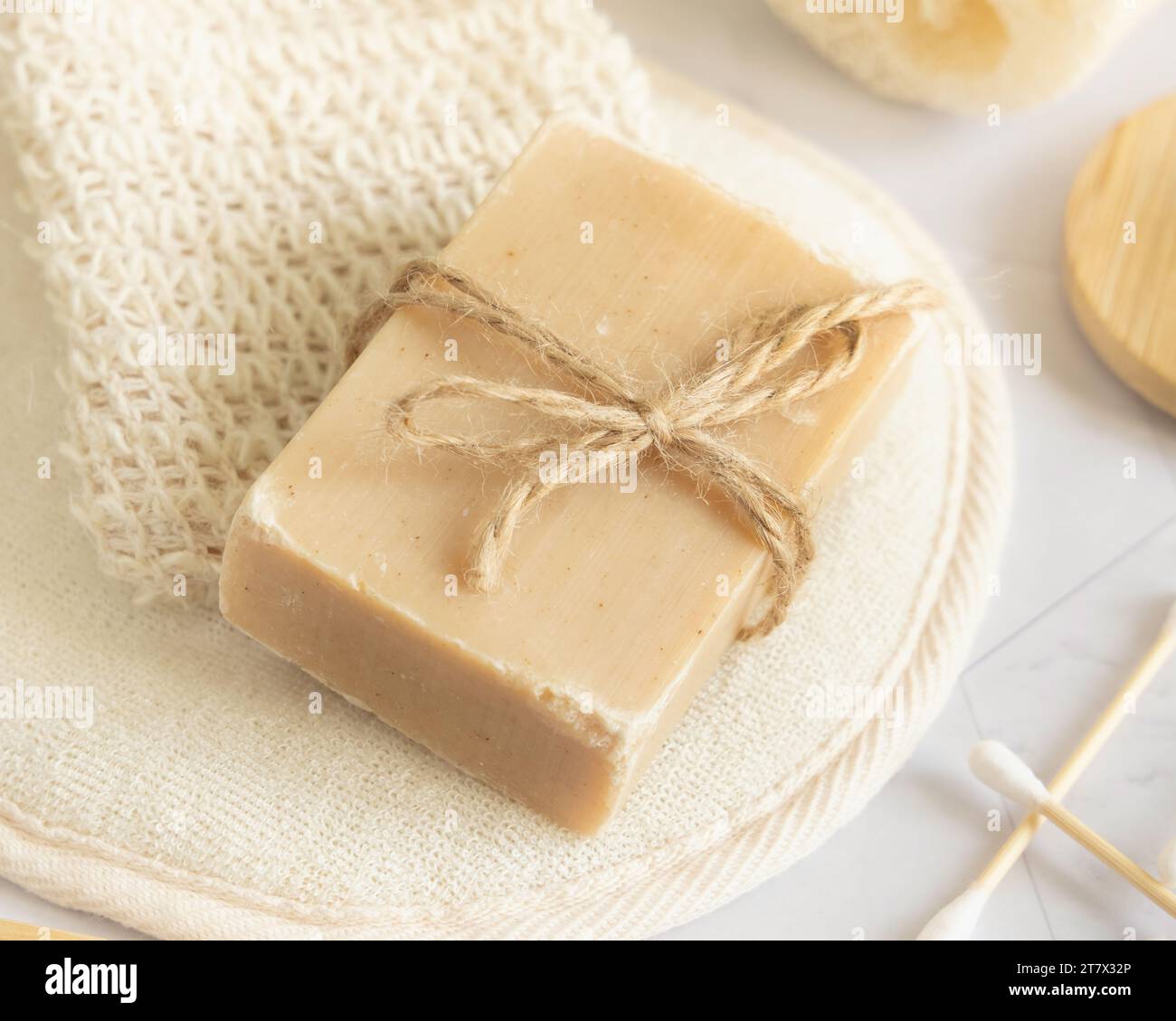 Beige handmade soap bar on sisal soap saver bag on white marble table close up, copy space. Natural herbal products for face and body care Stock Photo
