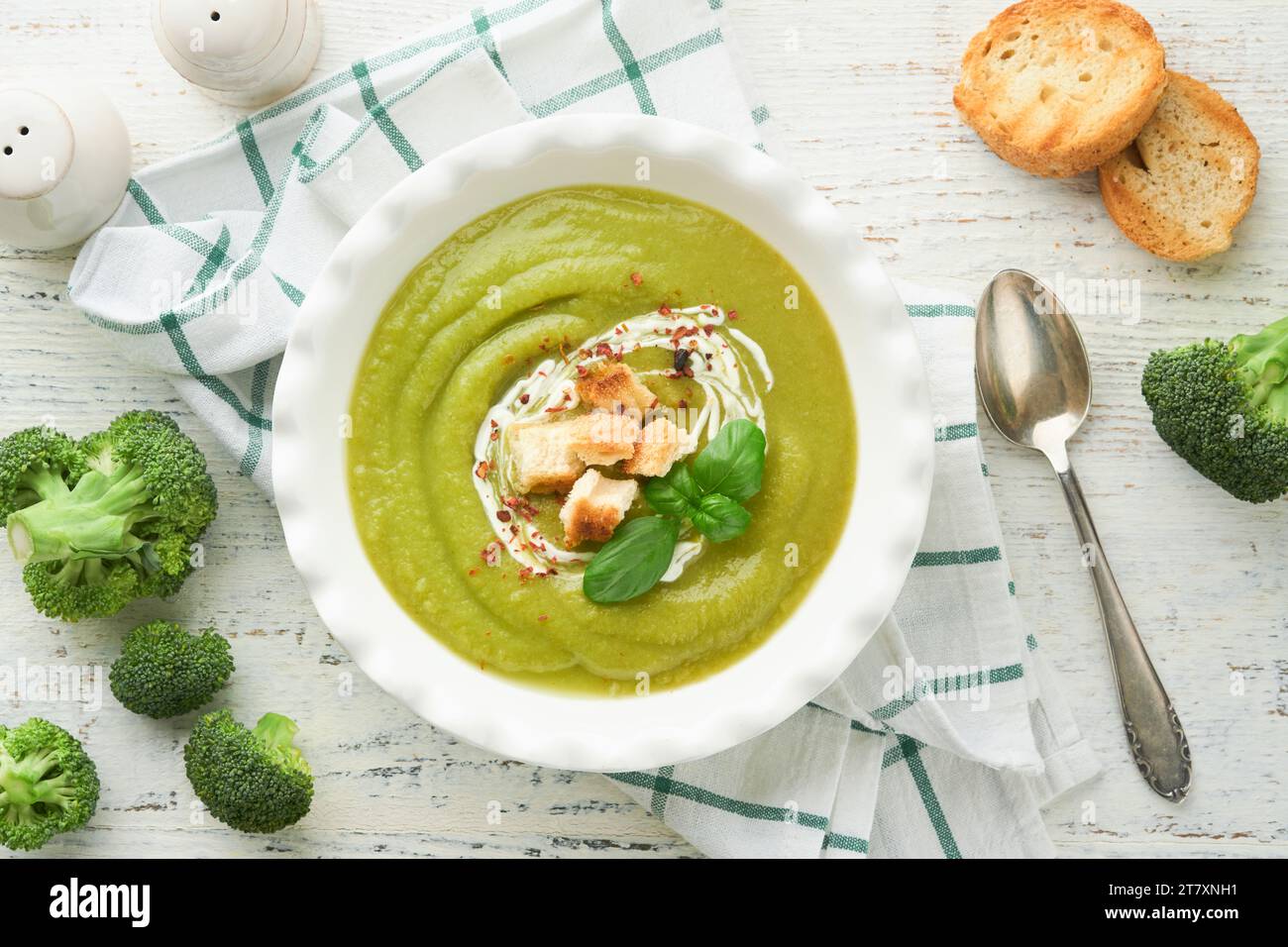 Broccoli cream soup. Fresh homemade broccoli soup in white plate with seasonings, parsley, basil and pieces of toasted bread on rustic white wooden ba Stock Photo