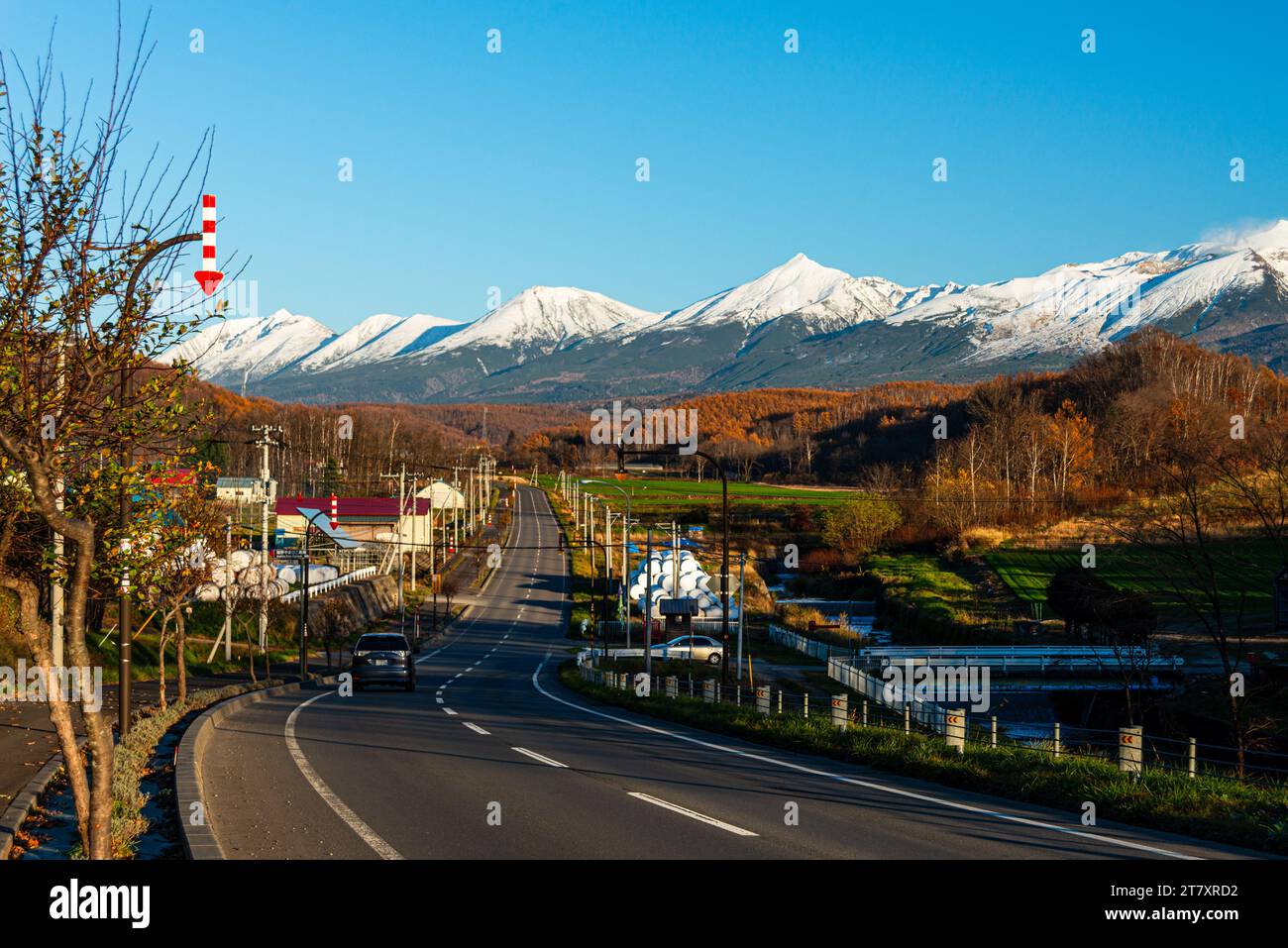 Alpine panorama of rural area with highway leading to the snowy Tokachi mountain range in Hokkaid , Japan, Asia Stock Photo