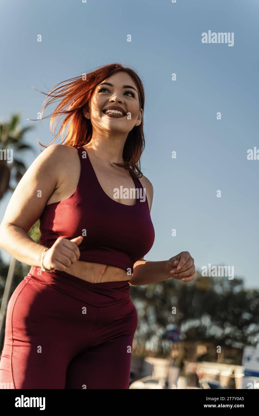 A vibrant woman enjoys a running session on a city park, showcasing her ...