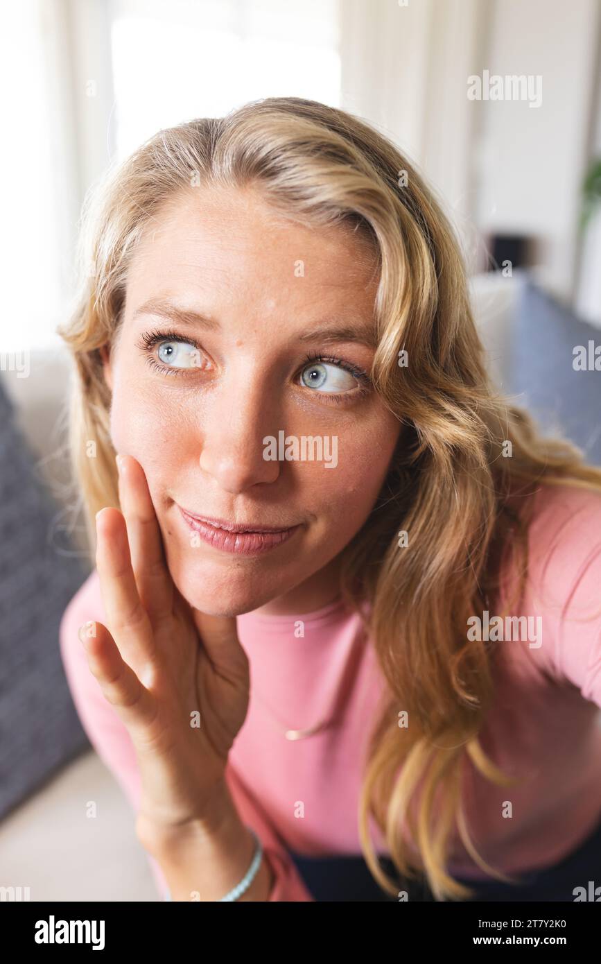 Happy blonde caucasian woman having video call and looking right in sunny living room Stock Photo