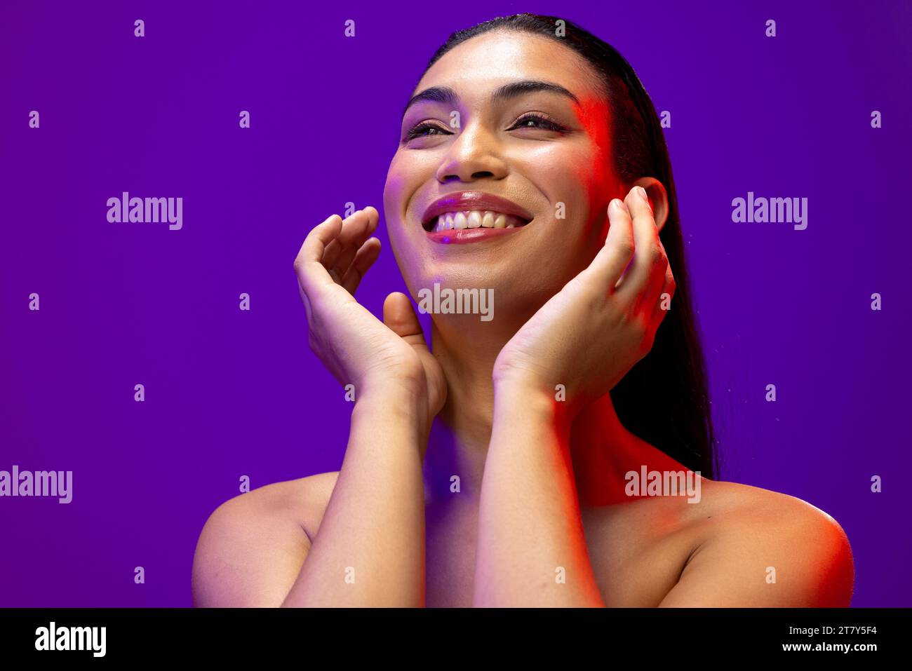 Portrait of smiling biracial woman with dark hair, red lips and eye make up on neon background Stock Photo