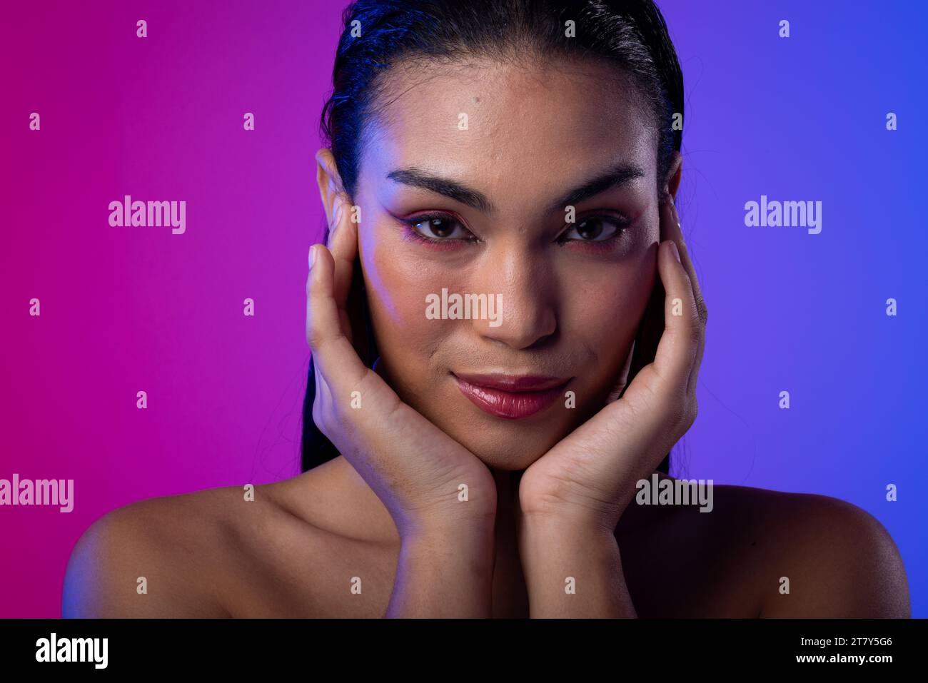 Biracial woman with dark hair, hands to face, red lips, eyeshadow make up on neon background Stock Photo