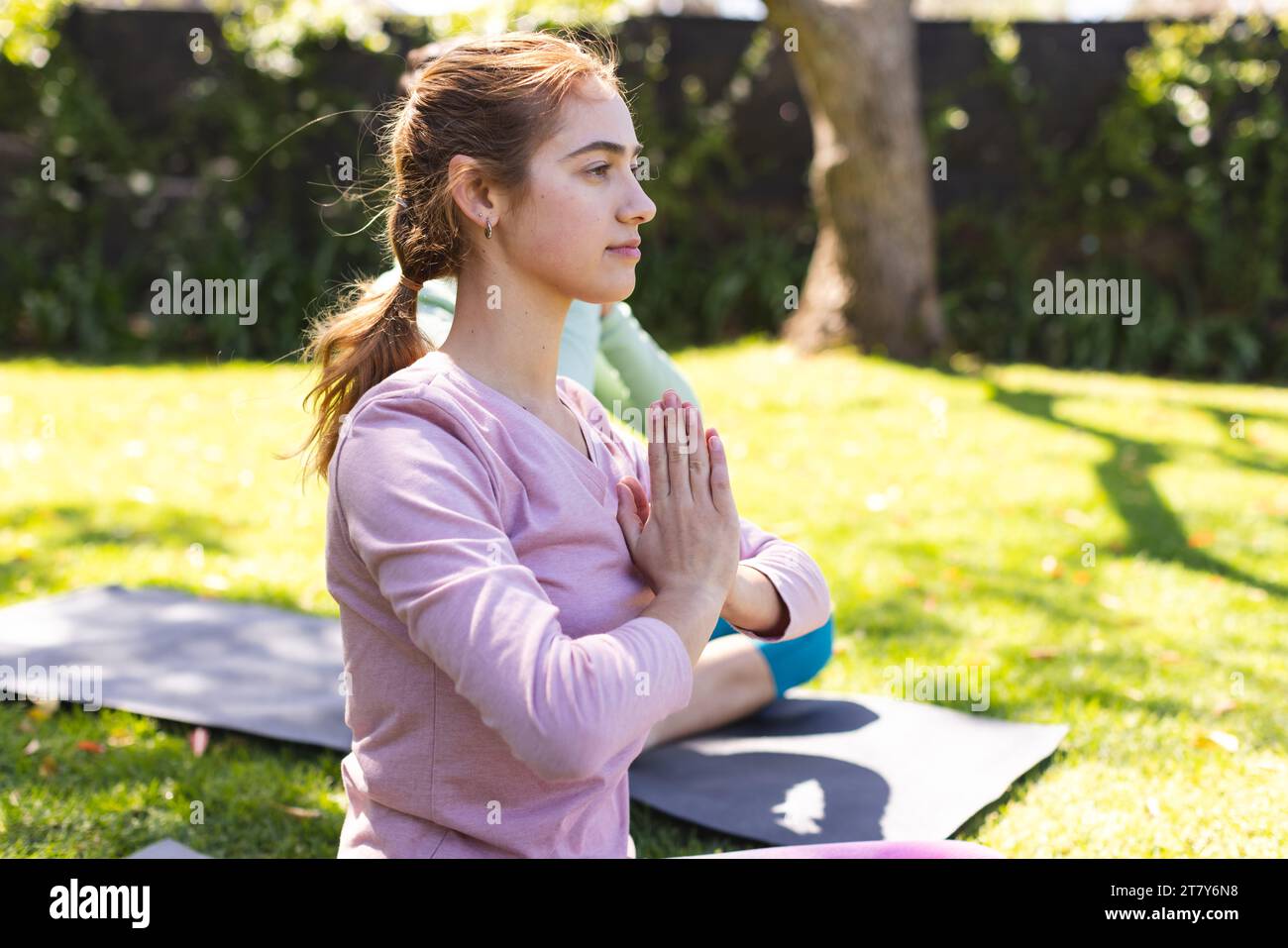 Focused biracial woman practicing yoga meditation sitting with friend in sunny garden, copy space Stock Photo