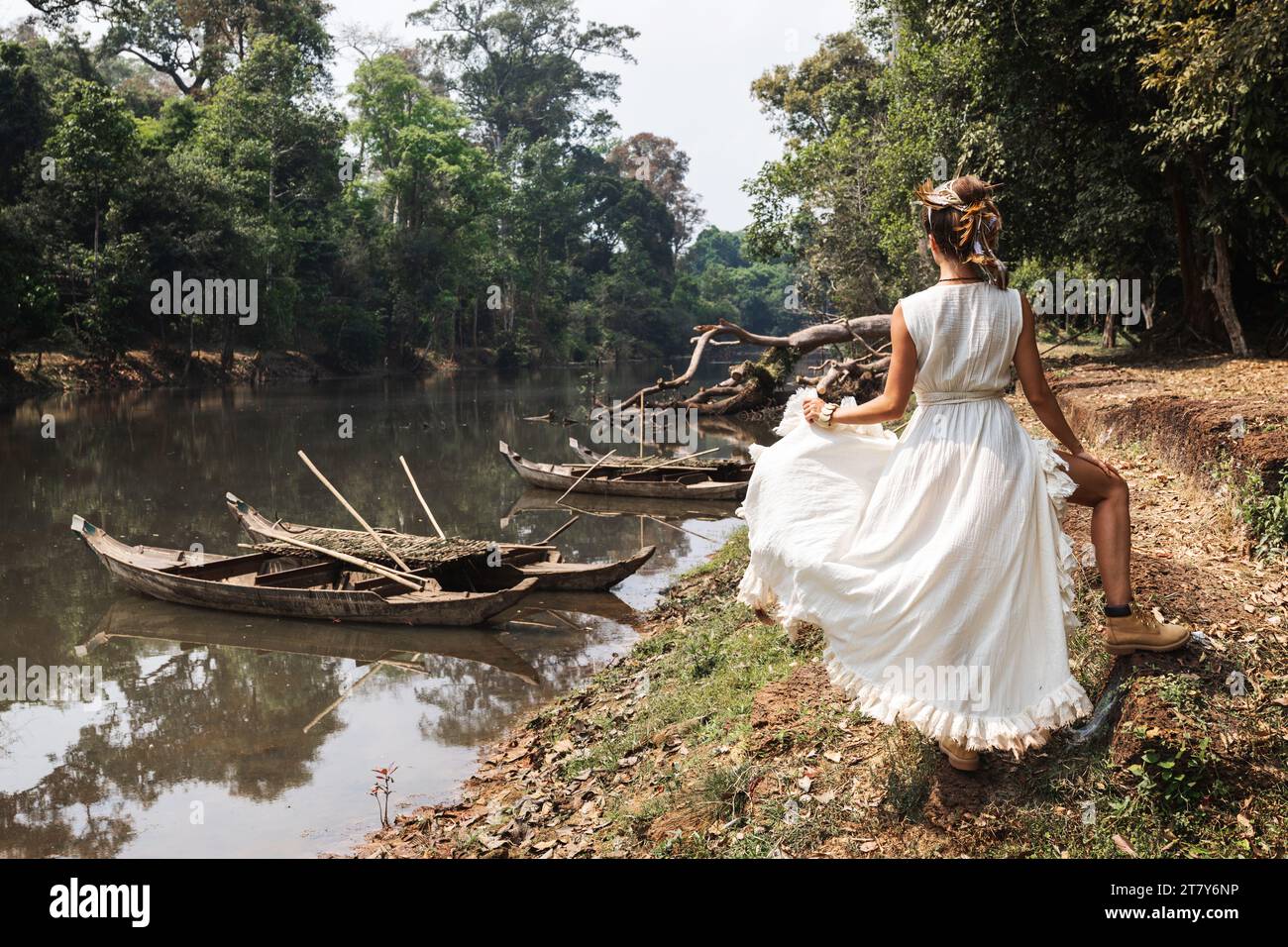 Woman wearing white robe dress posing near river with old wooden boats ...