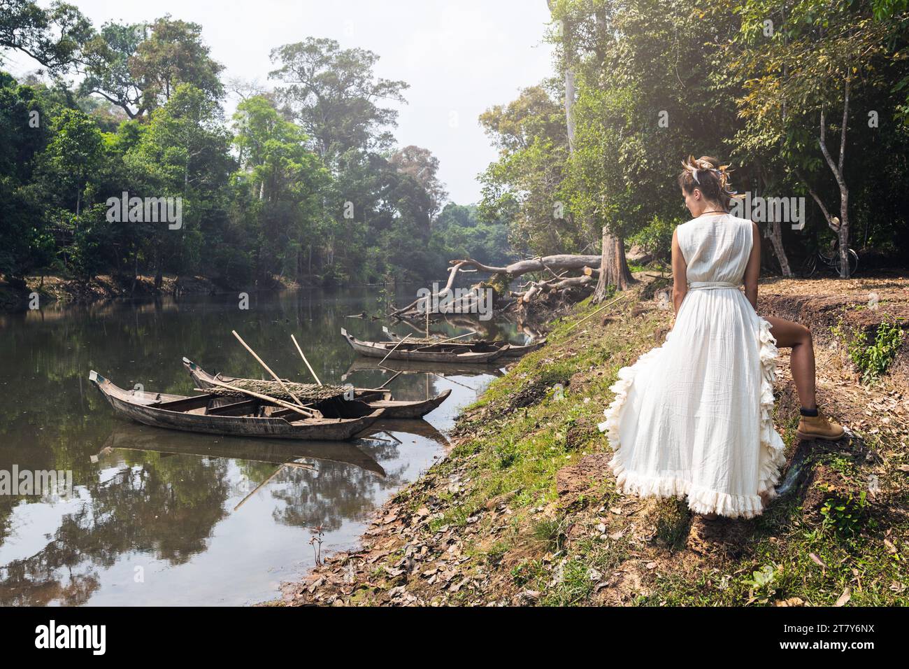 Woman wearing white robe dress posing near river with old wooden boats ...