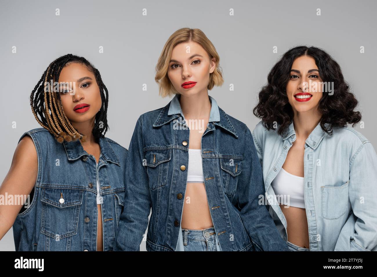 three attractive multiracial women in denim clothes looking at camera on grey, group portrait Stock Photo