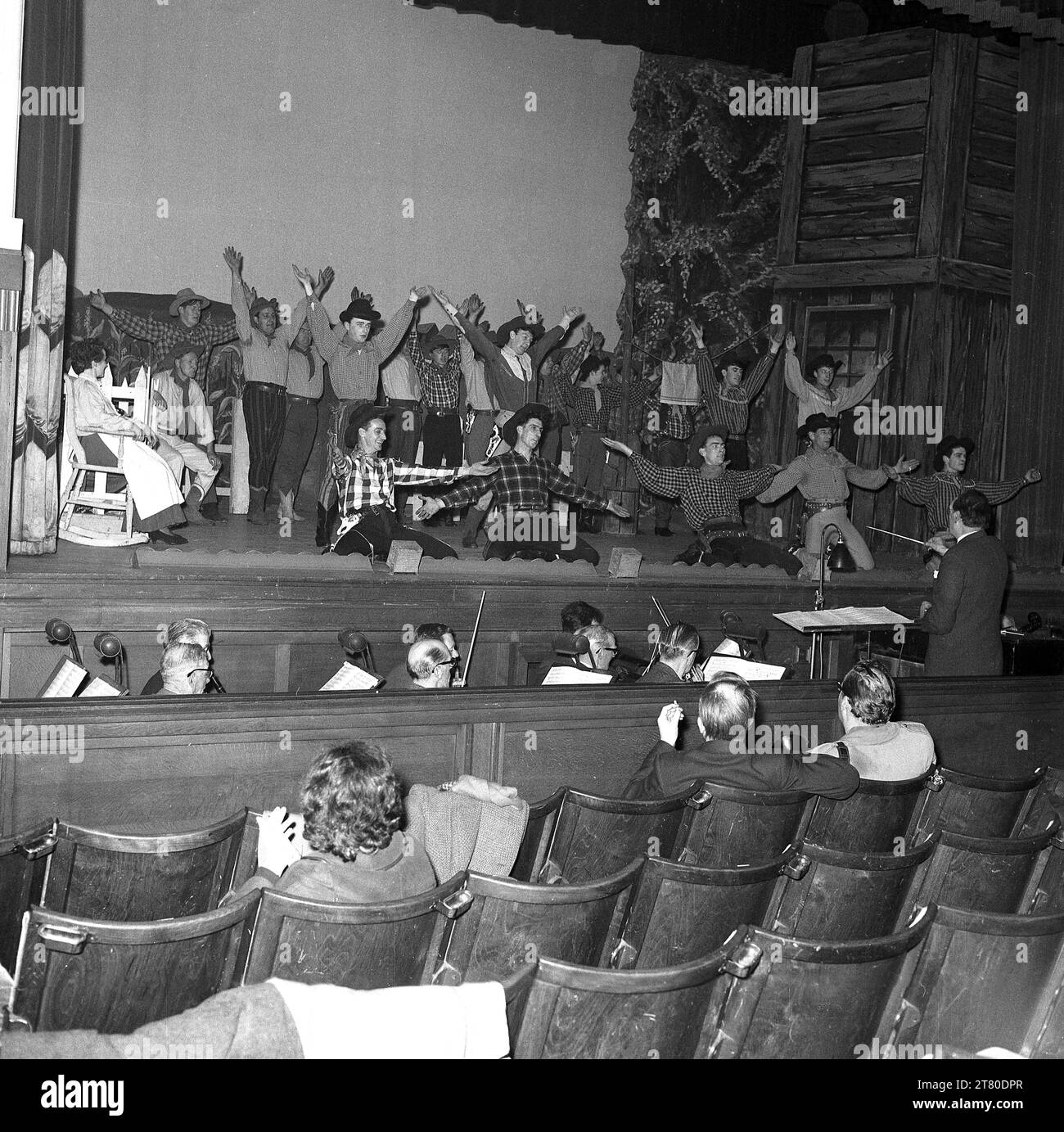 1960s, historical, performers on stage in the musical Oklahoma, with orchestra and conductor in the pit infront of the stage, Kelty, Scotland, UK. Traditional wooden seats for the audience. Written by Rodgers & Hammerstein, the musical tells the story of an early 20th century american farm girl and her rival suitors. Stock Photo