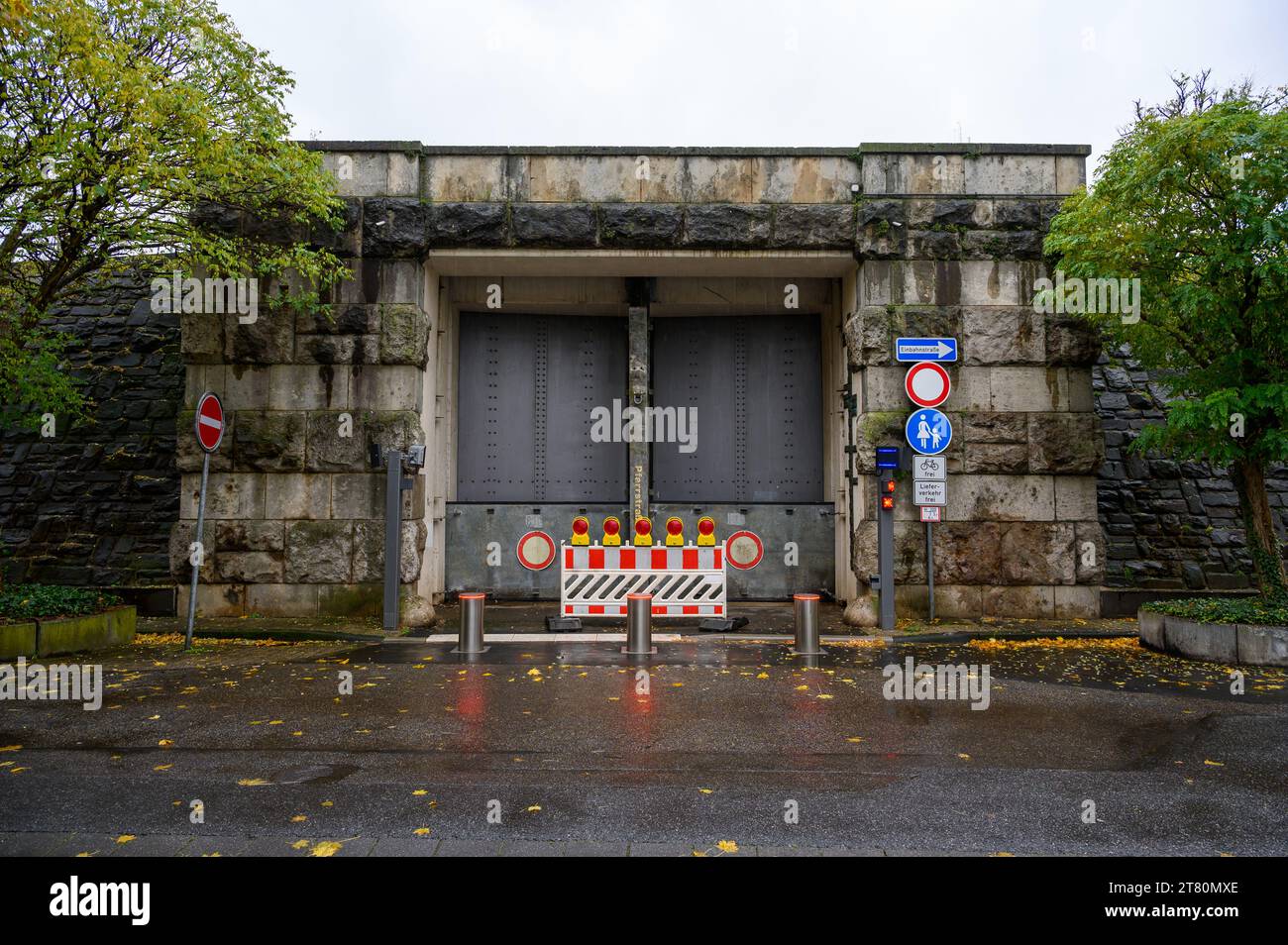 A heavy steel door sits in a stone frame of a dam protecting against flooding. The gate is closed with red lights and barriers protruding from the gro Stock Photo