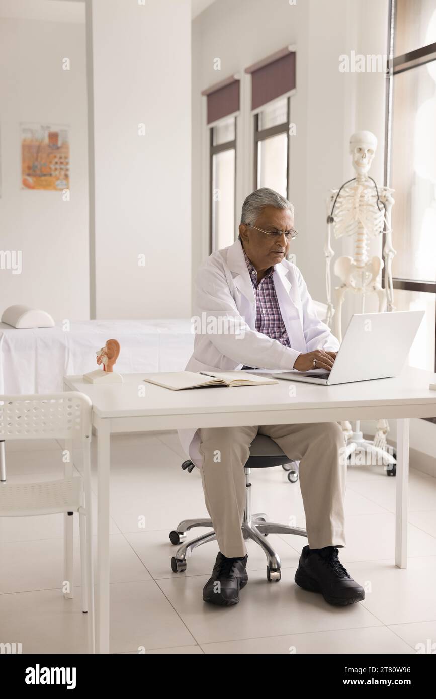 Serious elderly Indian practitioner man working at laptop Stock Photo