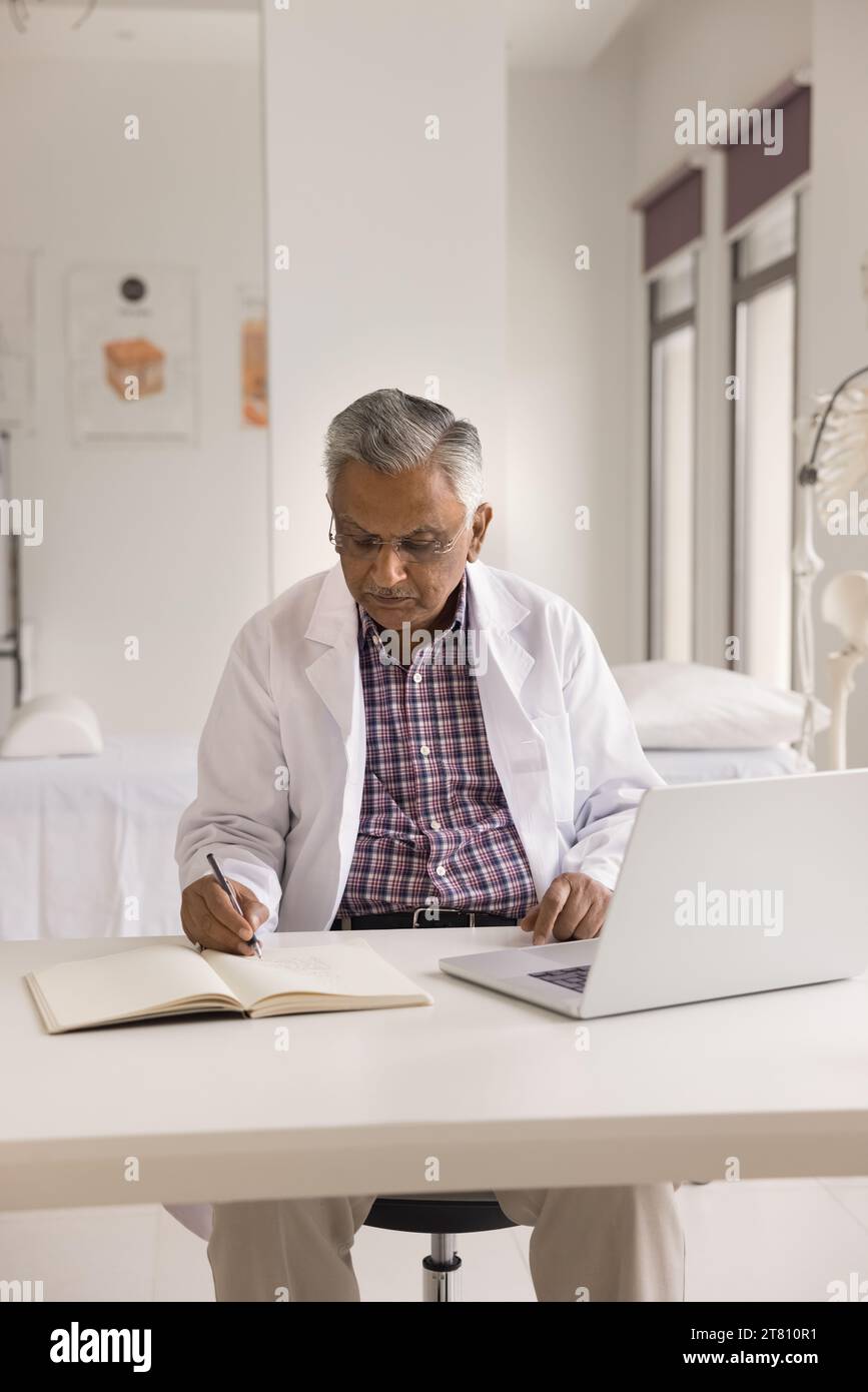 Serious focused older Indian practitioner man writing medical notes Stock Photo