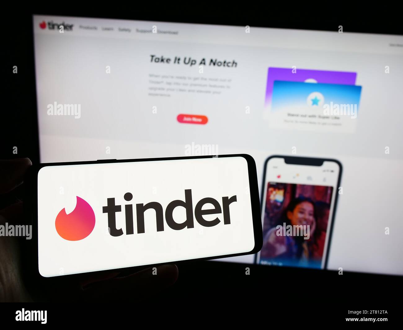 Person holding cellphone with logo of US online dating app Tinder in front of company webpage. Focus on phone display. Stock Photo