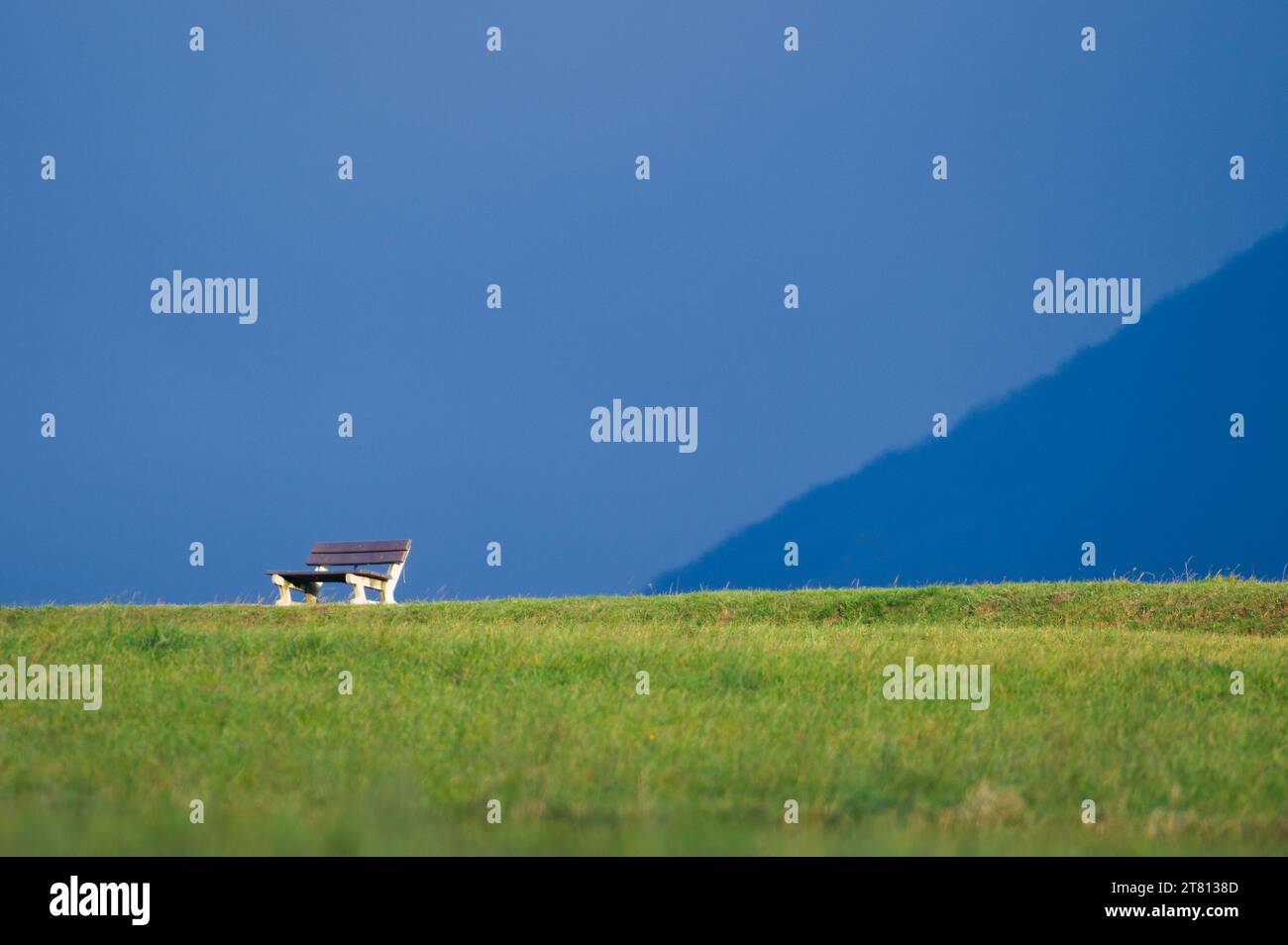 Lonely empty bench on the horizon in nature. Loneliness concept. Isolated on blue background. Negative space for placement of text. Stock Photo