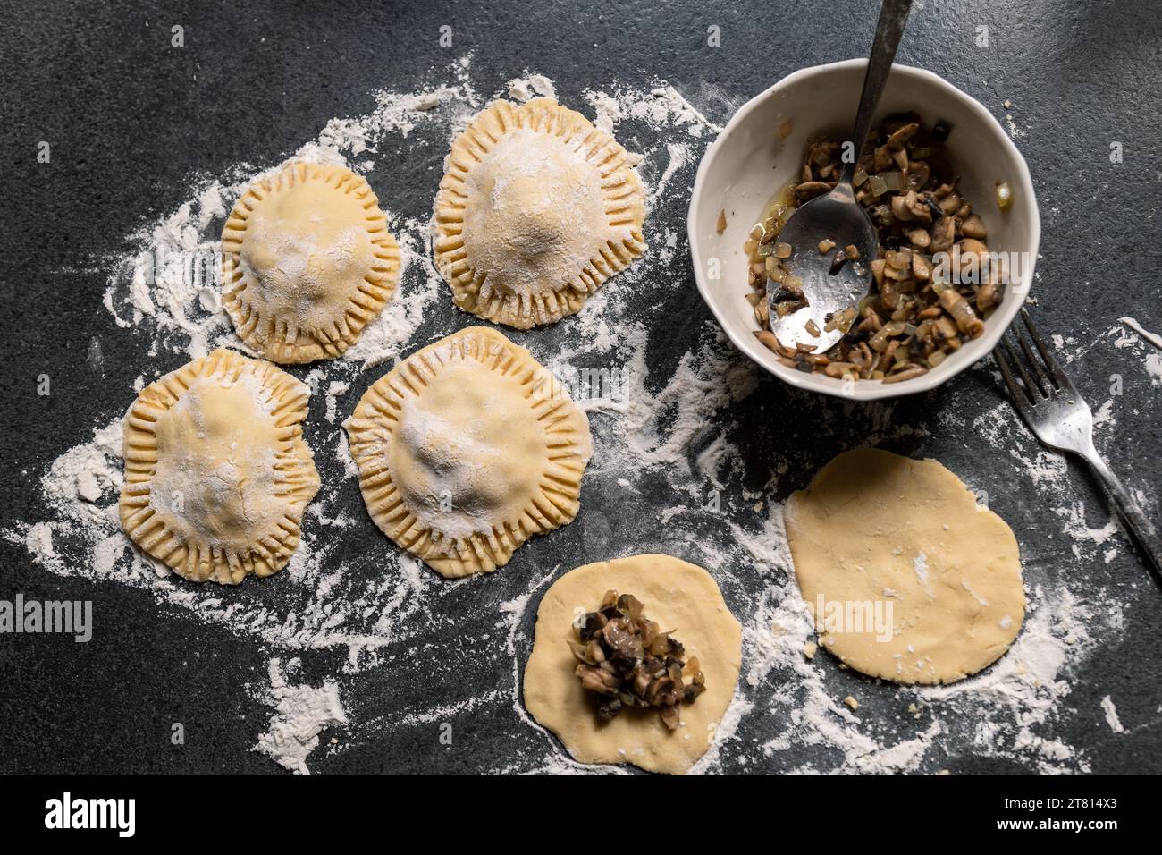 Preparation of gluten-free dumplings stuffed with mushrooms and onions. Dark gray countertop sprinkled with flour. Homemade. Stock Photo