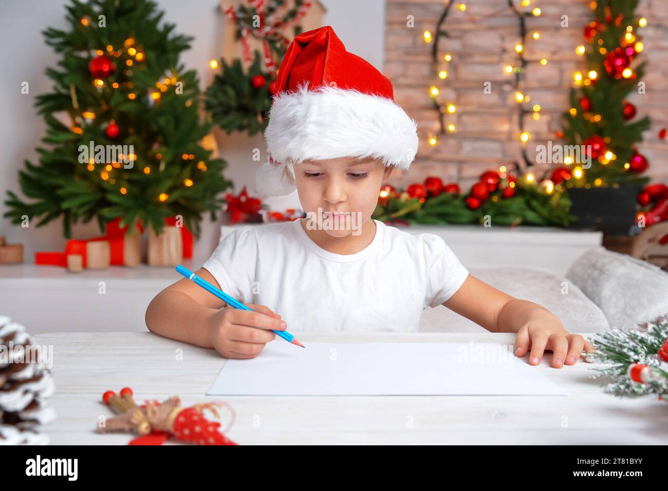 Girl in Christmas hat drawing and writing on blank paper, festive background with Christmas trees, lights, and decorations. Creative holiday Stock Photo