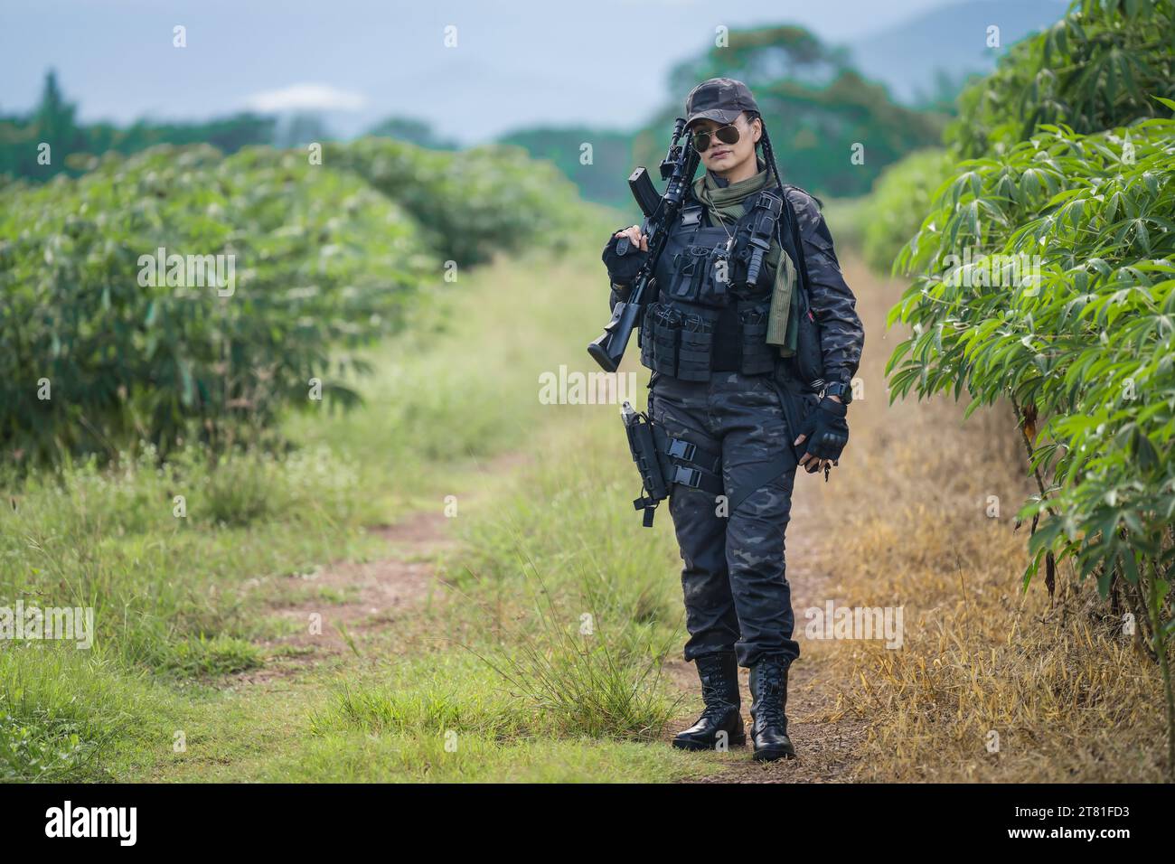 A military soldier stands ready for action with an assault rifle in hand, surrounded by lush shrubbery in the background Stock Photo