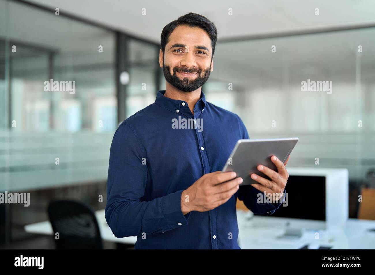 Smiling Indian businessman using tab computer working standing in office. Stock Photo