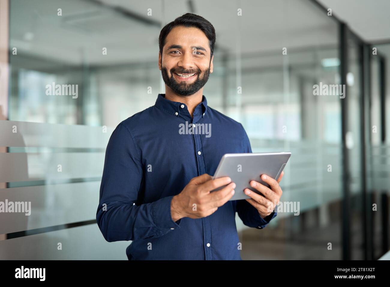 Smiling Indian businessman using tab computer working standing in office. Stock Photo