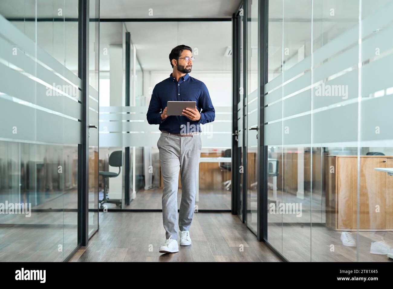 Confident Indian business man looking aside walking with tablet in office. Stock Photo
