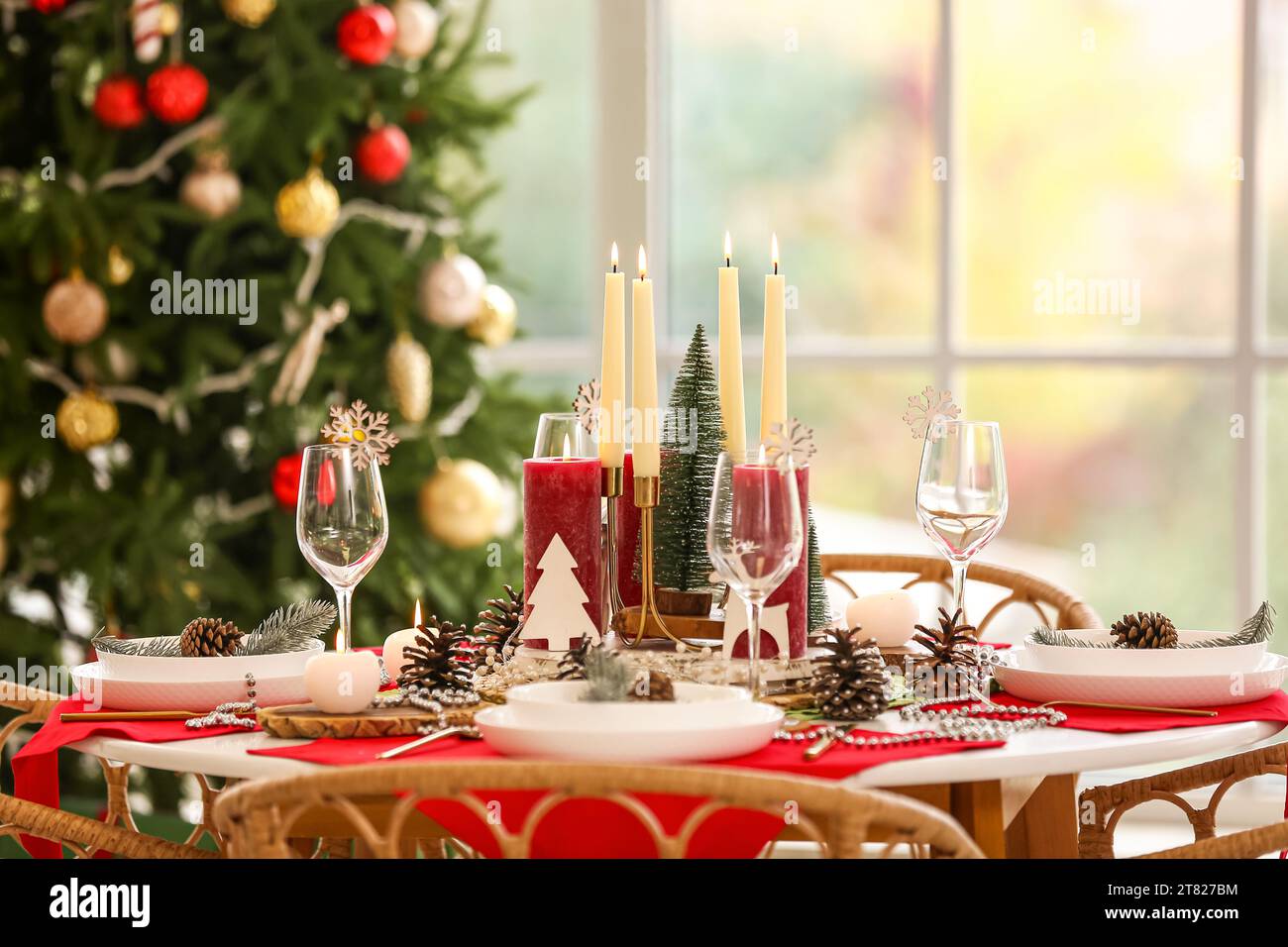 Christmas table setting with burning candles and fir cones in room ...