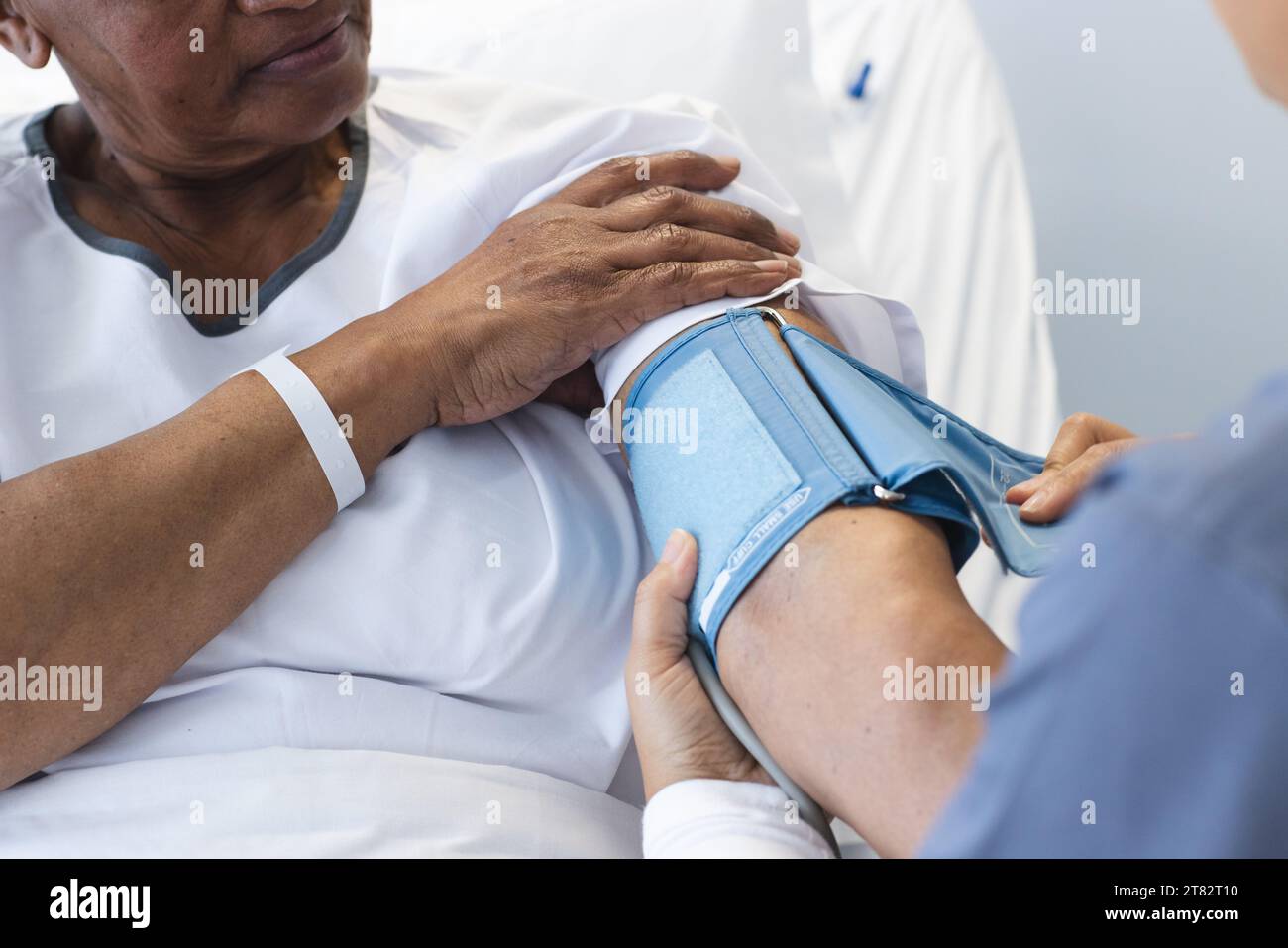 Diverse female doctor testing blood pressure of senior female patient in hospital room Stock Photo