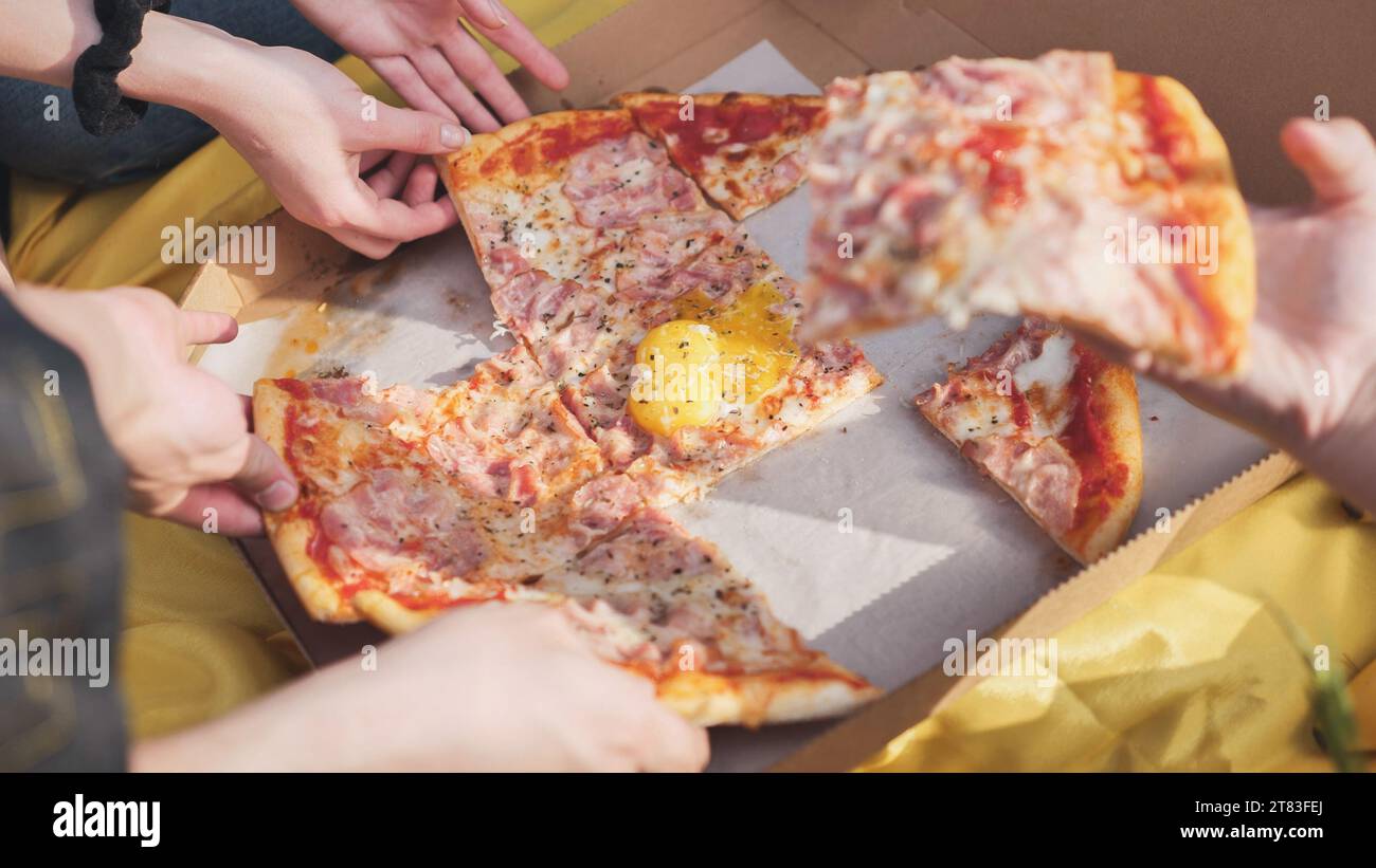 Young students' hands reach for the pizza. Stock Photo