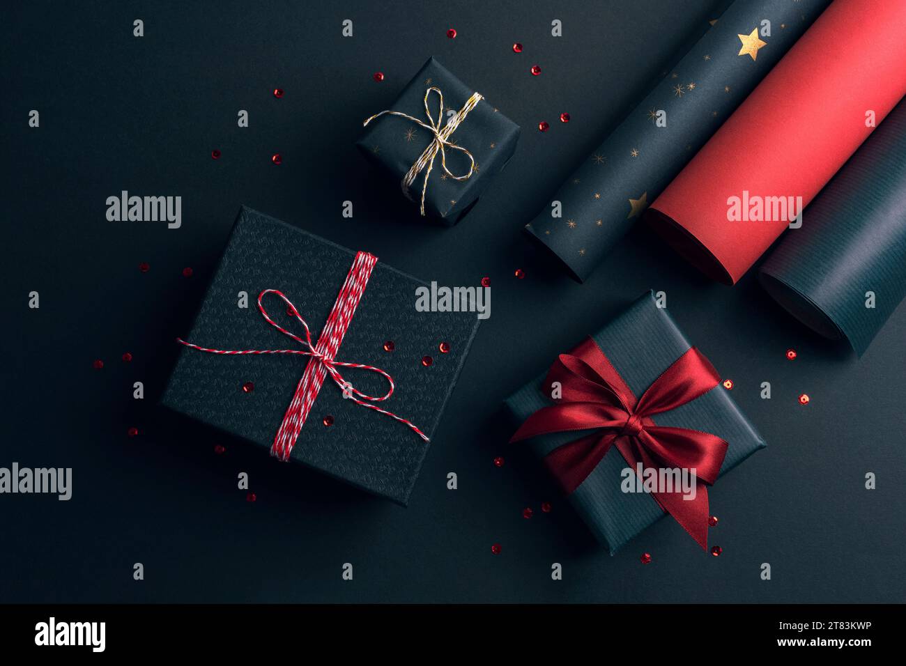 Gift boxes packaging with red bow and rolls of wrapping paper on black ...