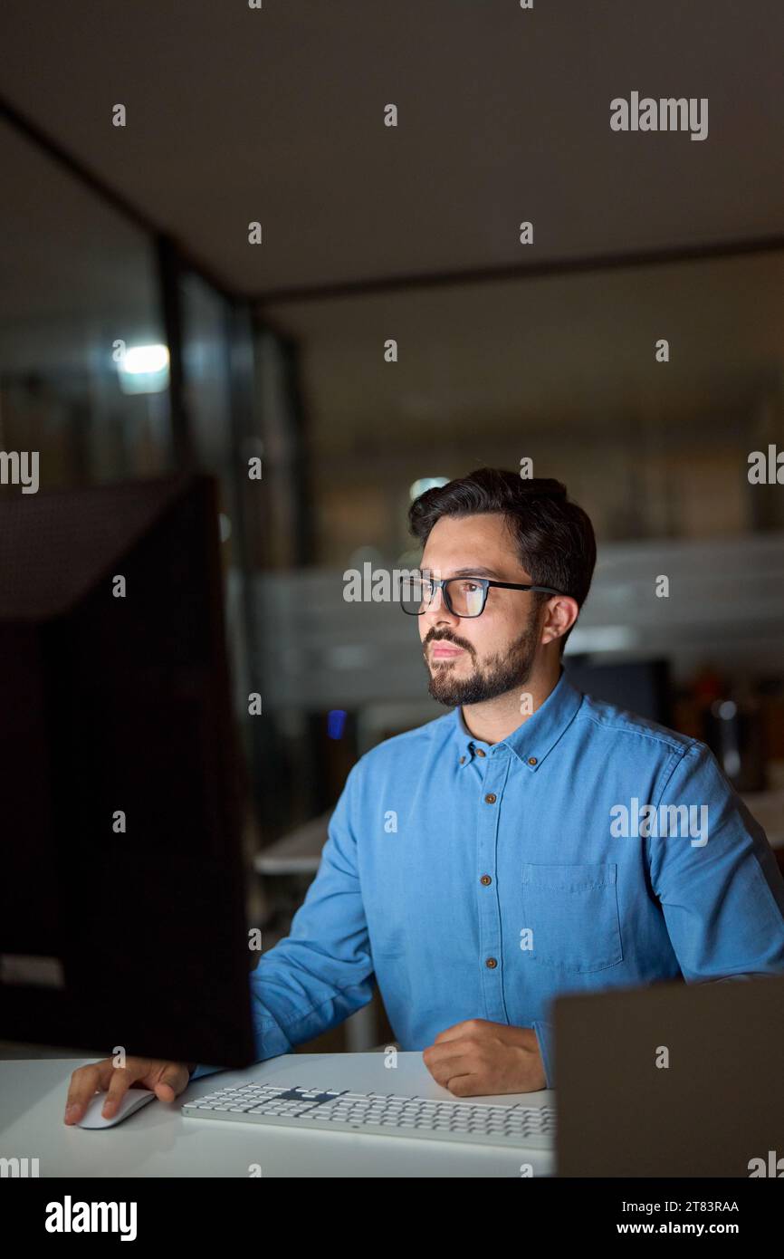 Busy young business man using computer working late in office. Vertical. Stock Photo