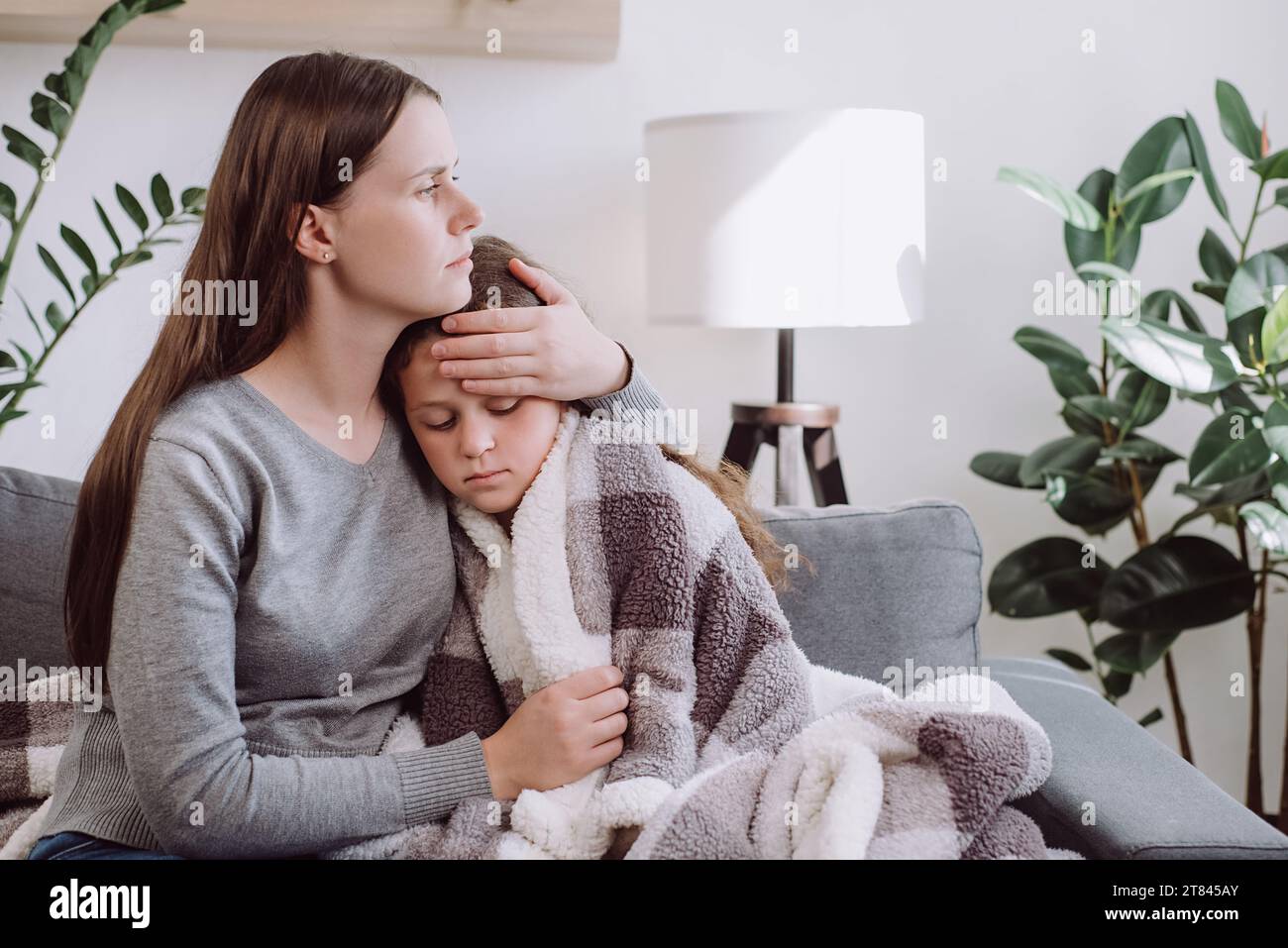 Caring young mother hugging, sick upset little daughter covered blanket