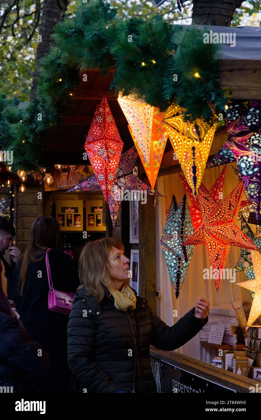 A woman looking at an festive display of  Diwali Star Lights and Lanterns at a Christmas Market stand, England, Yorkshire, UK. Stock Photo