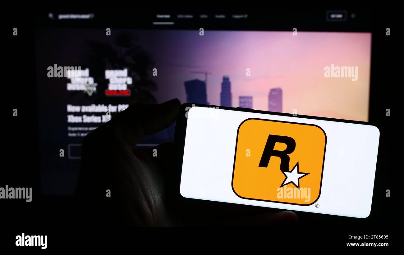 Person holding mobile phone with logo of American video game publishing company Rockstar Games Inc. in front of web page. Focus on phone display. Stock Photo