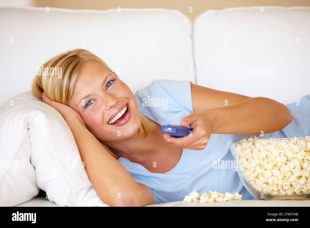 Portrait, funny and watching tv with woman, popcorn and remote with happiness, relax and comedy. Face, person and girl on a couch, snack and streaming Stock Photo