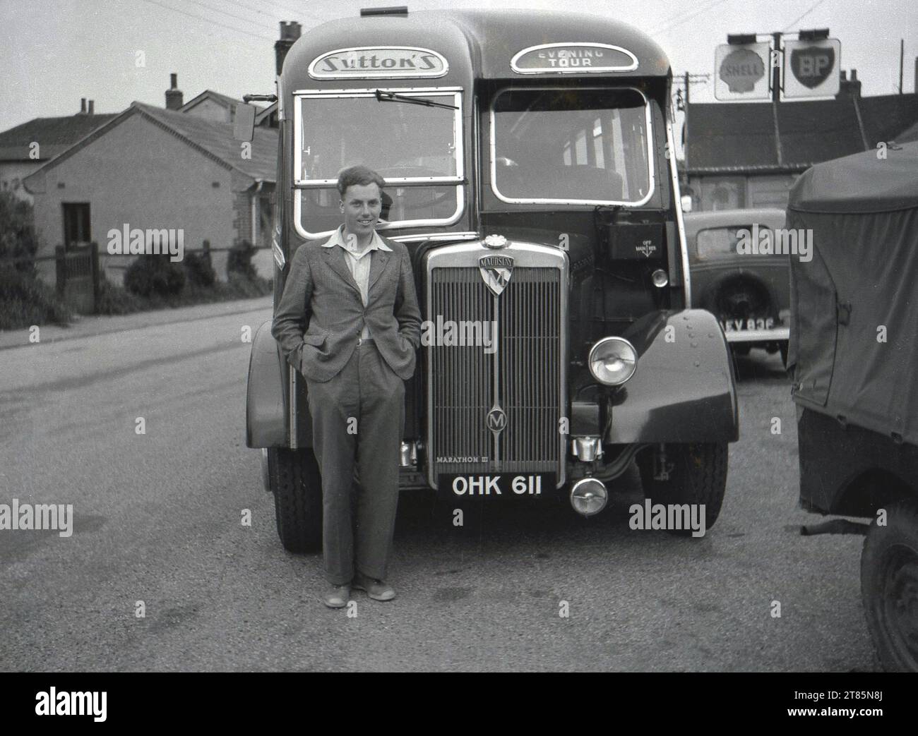 1950s, historical, outside a garage a man standing infront of a motor coach of the era, a Maudslay Marathon III operated by Sutton's, providing as the sign says, An Evening Tour.  Before overseas package holidays in the late 1960s and 70s, in Britain people travelled to holiday destinations by coach and buses which distinctive and stylish body designs. The 1950s are considered the 'golden age' of coach travel. Stock Photo
