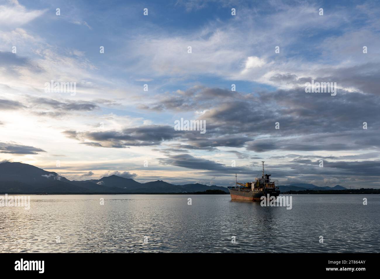 Old rusting cargo tanker sits anchored in beautiful remote port surrounded by mountains Stock Photo