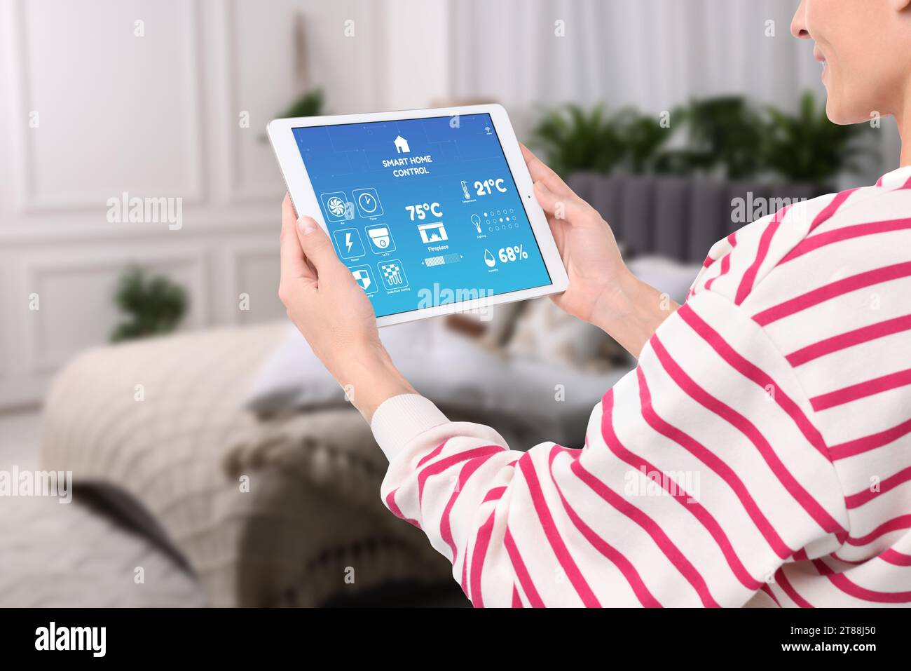 Woman using smart home control system via application on tablet indoors, closeup Stock Photo