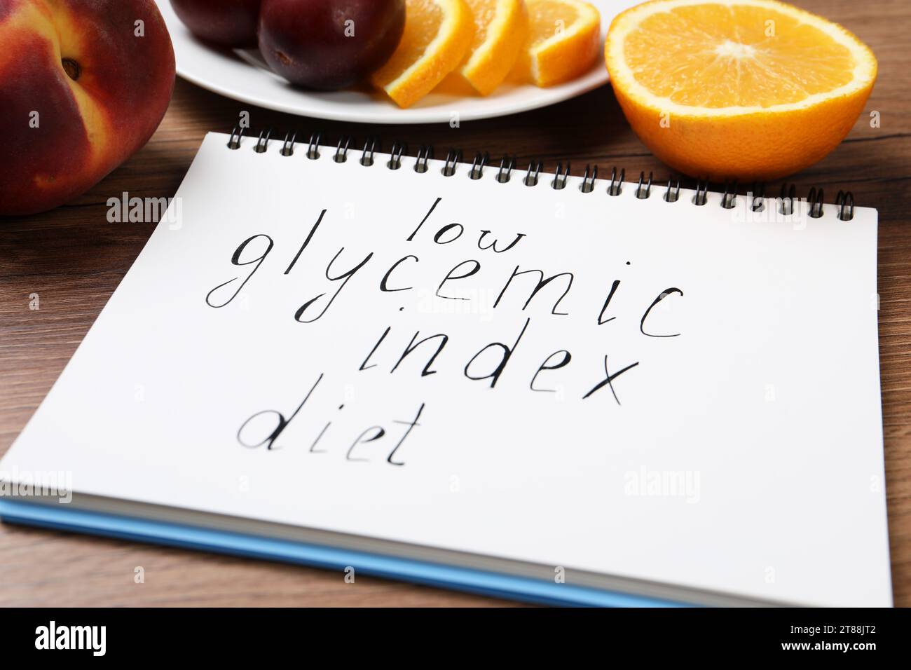 Notebook with words Low Glycemic Index Diet and fresh fruits on wooden table, closeup Stock Photo