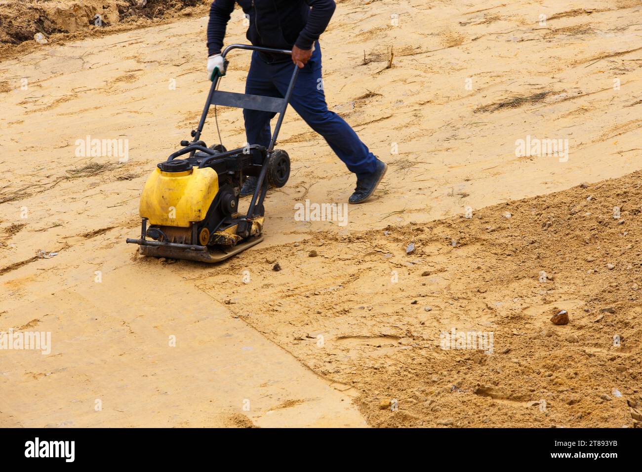 Worker using vibratory plate compactor for compaction sand during path