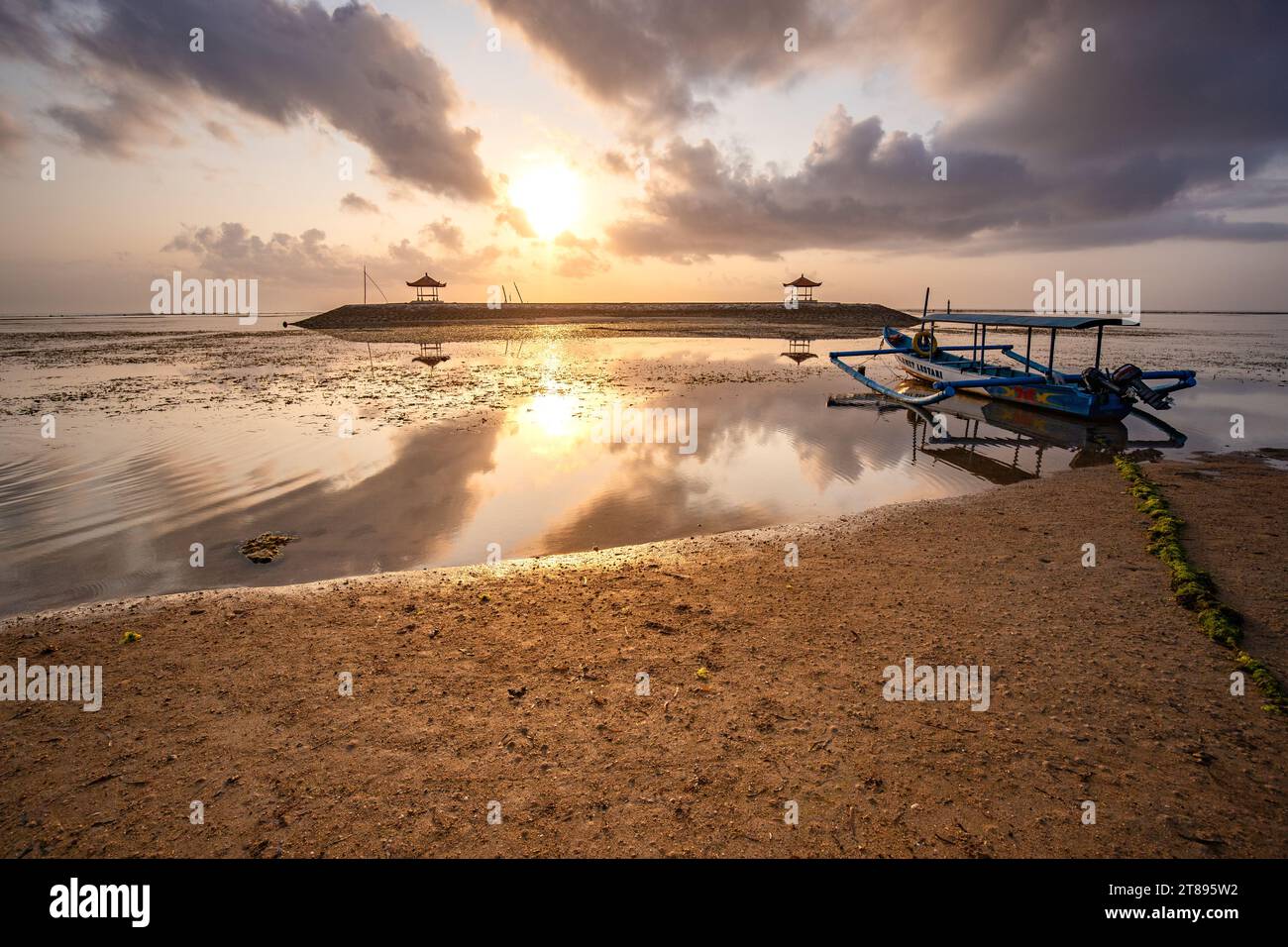 Sunrise at the sandy beach of Sanur. Temple in the water. Traditional fishing boat, Jukung on the beach. Hindu faith in Sanur on Bali. Dream island Stock Photo